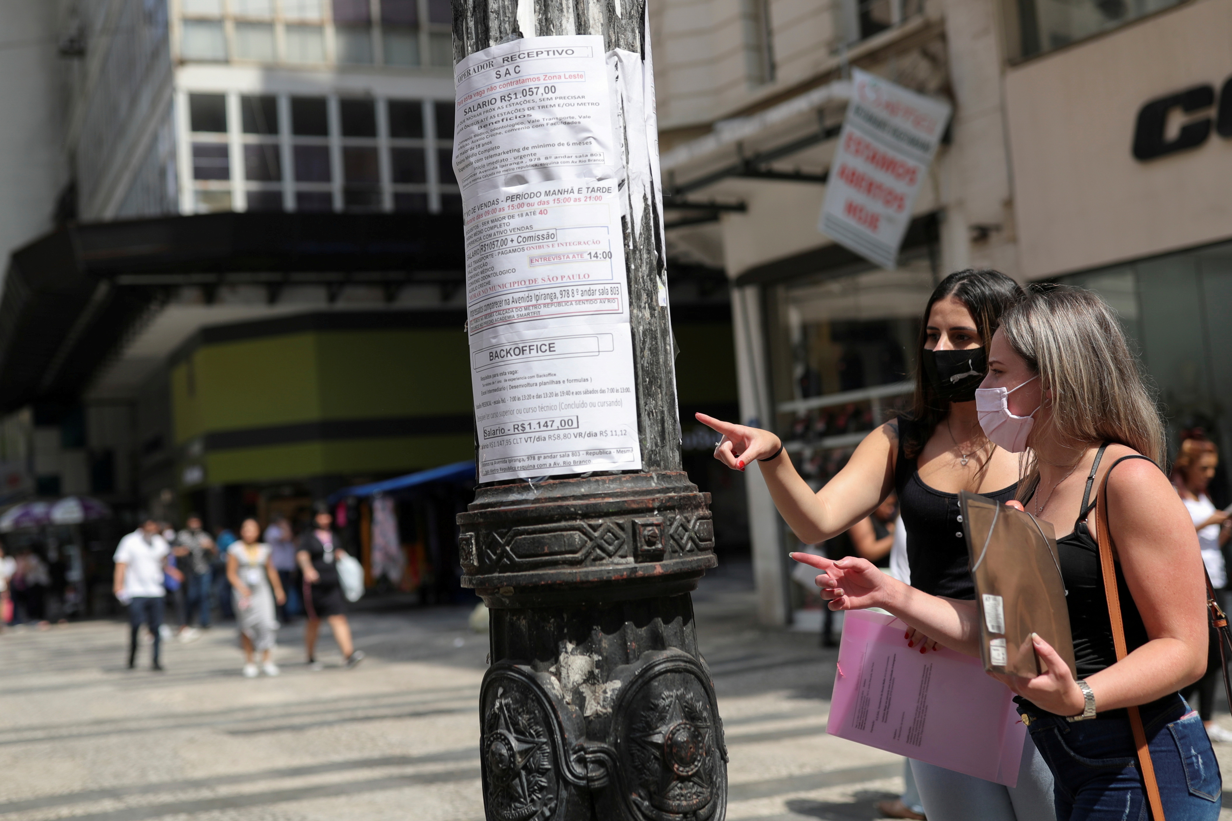 Women look at job listings posted on a light pole in downtown Sao Paulo