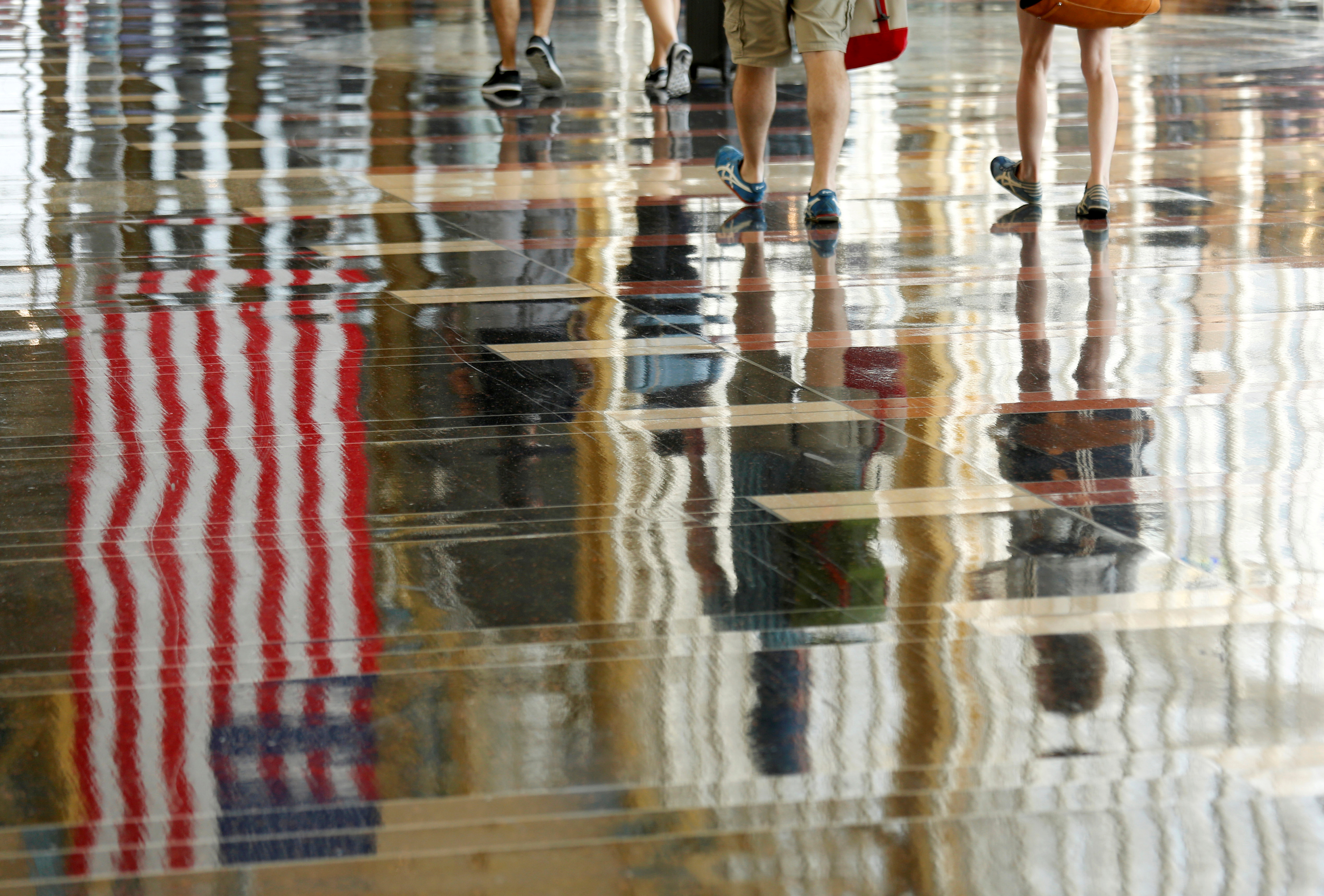 A U.S. flag is reflected on the floor as passengers make their way through Reagan National Airport in Washington, U.S., July 1, 2016. REUTERS/Kevin Lamarque/File Photo/File Photo
