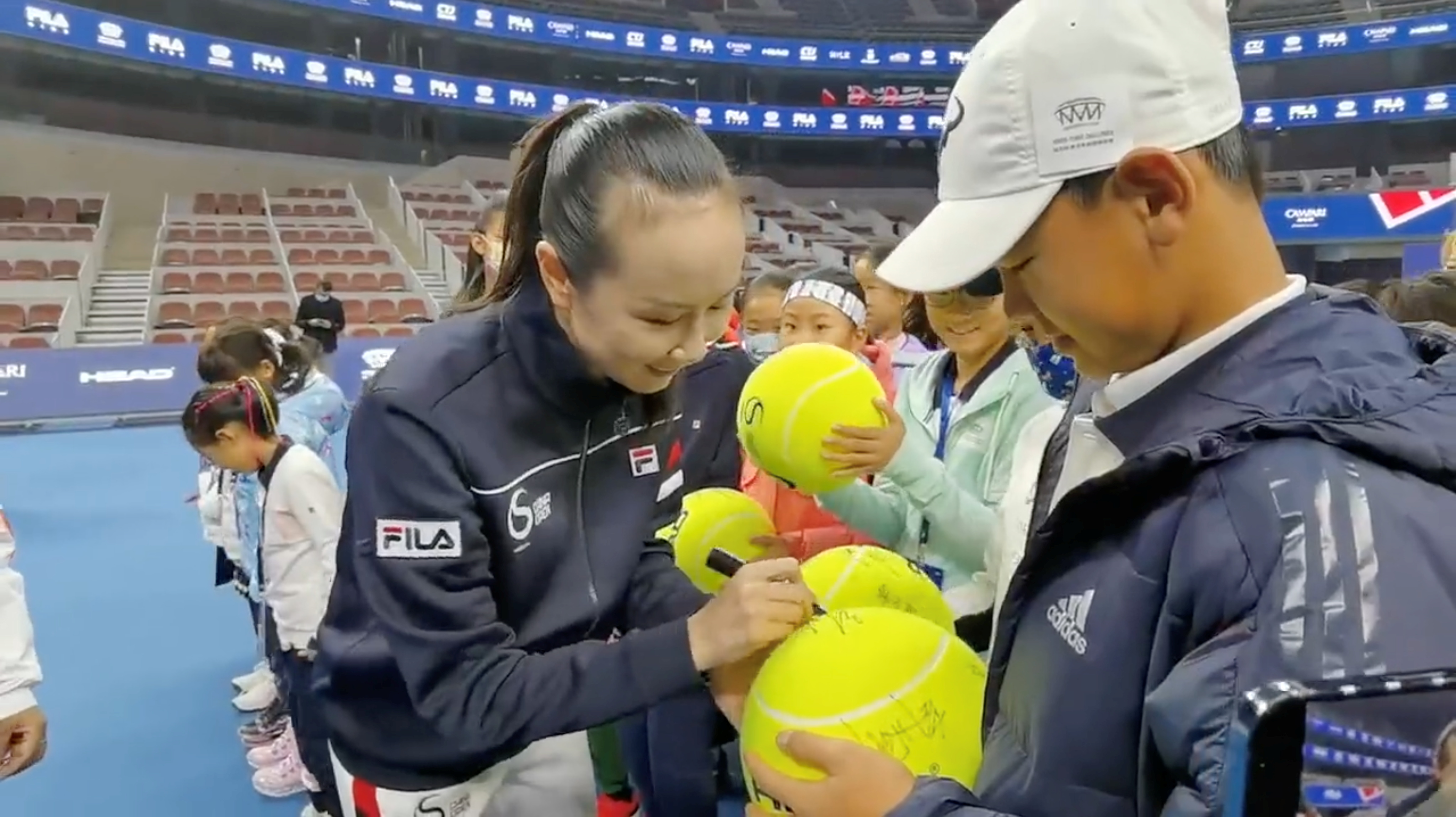 Chinese tennis player Peng Shuai signs large-sized tennis balls at the opening ceremony of Fila Kids Junior Tennis Challenger Final in Beijing, China November 21, 2021, in this screen grab obtained from a social media video. TWITTER @QINGQINGPARIS via REUTERS