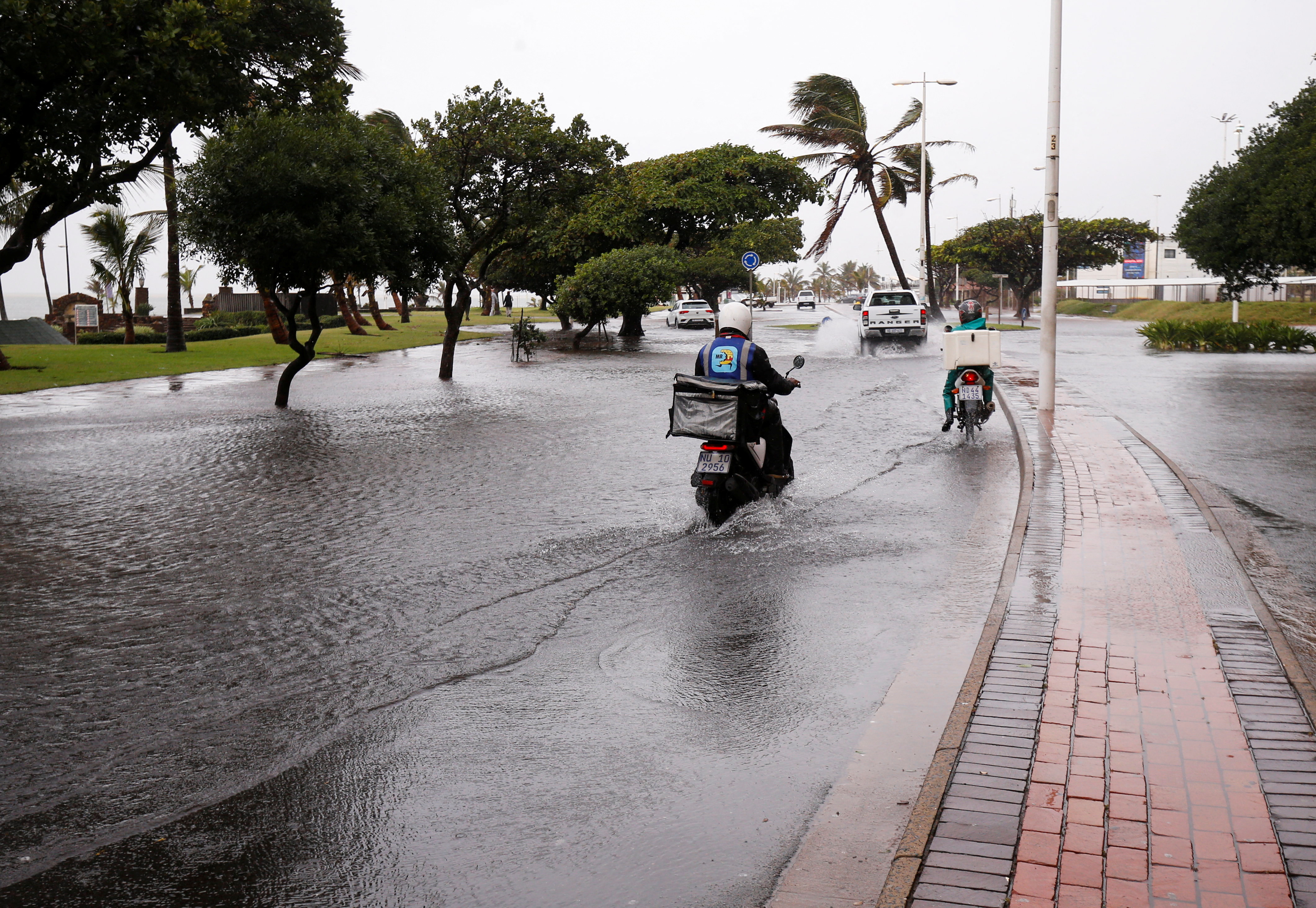Delivery bikes ride along a waterlogged road on the beach front after heavy rains, in Durban