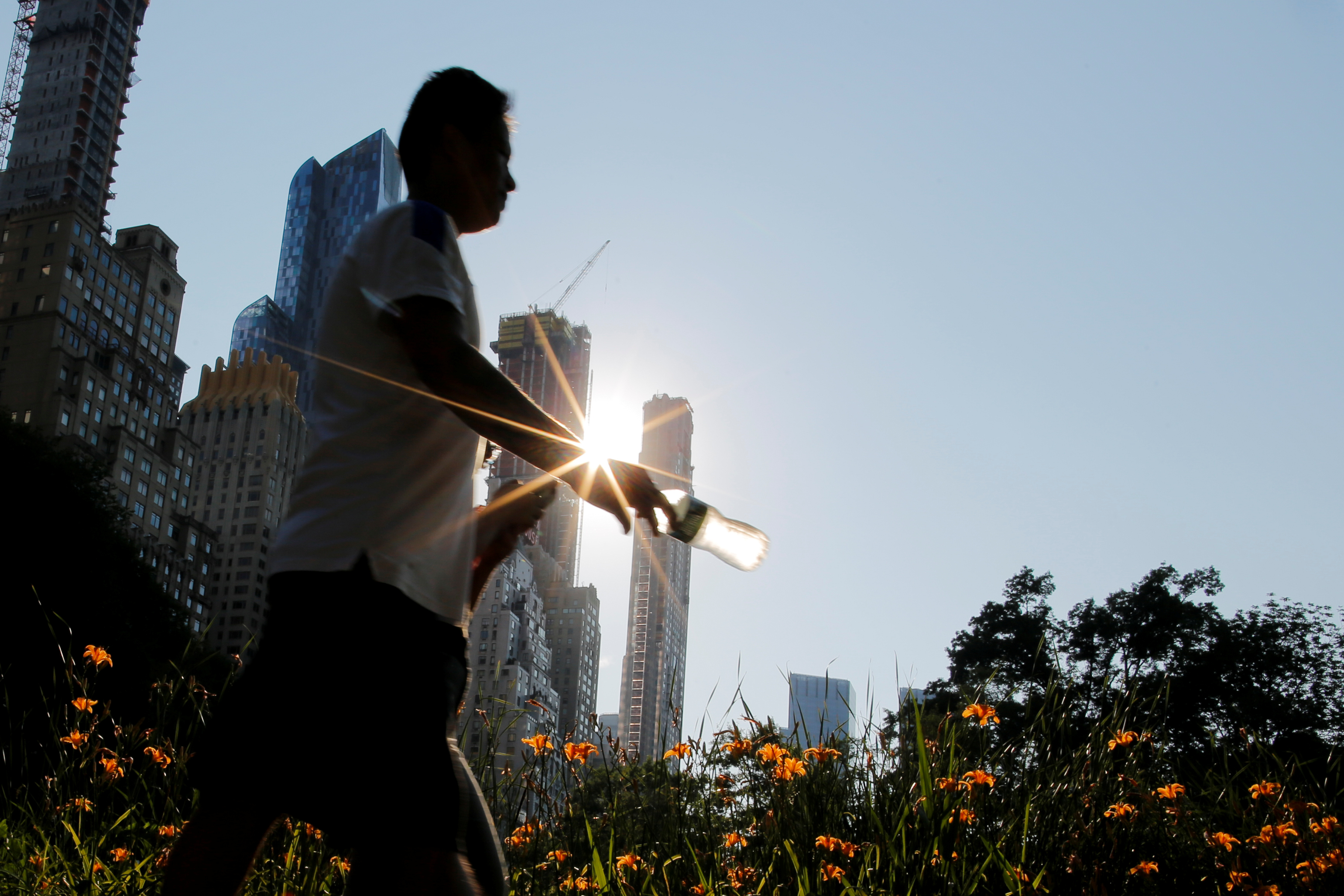 A man carries a bottle of water on a hot summer day in Central Park, Manhattan, New York