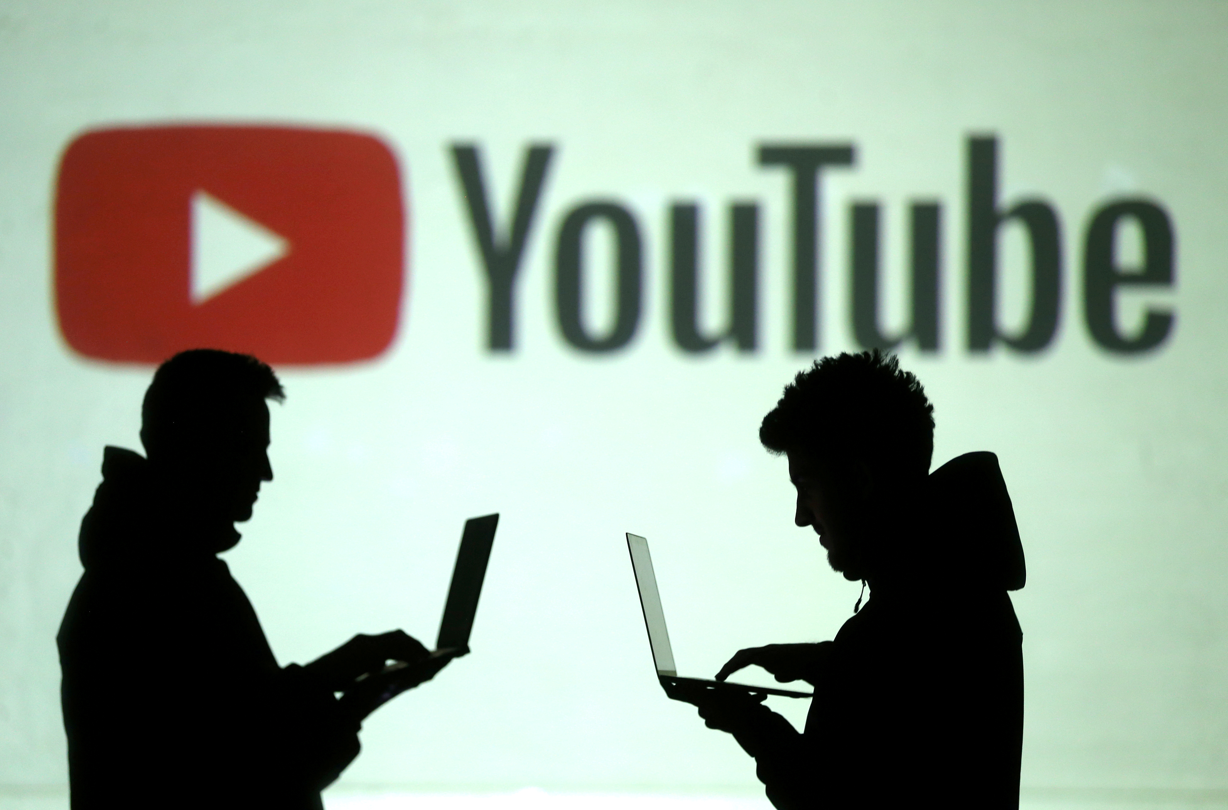 Silhouettes of mobile device users are seen next to a screen projection of Youtube logo in this picture illustration taken March 28, 2018.  REUTERS/Dado Ruvic/Illustration/File Photo