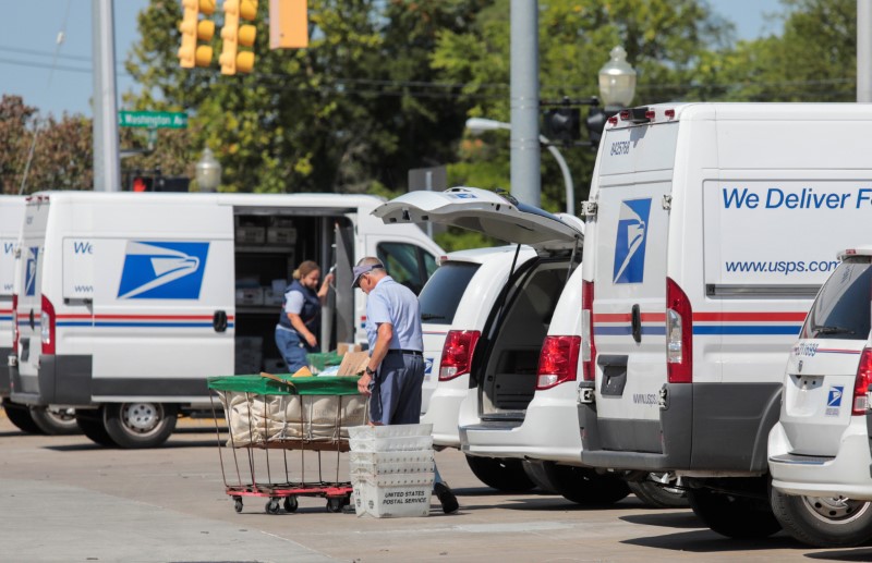 United States Postal Service (USPS) workers load mail into delivery trucks outside a post office in Royal Oak