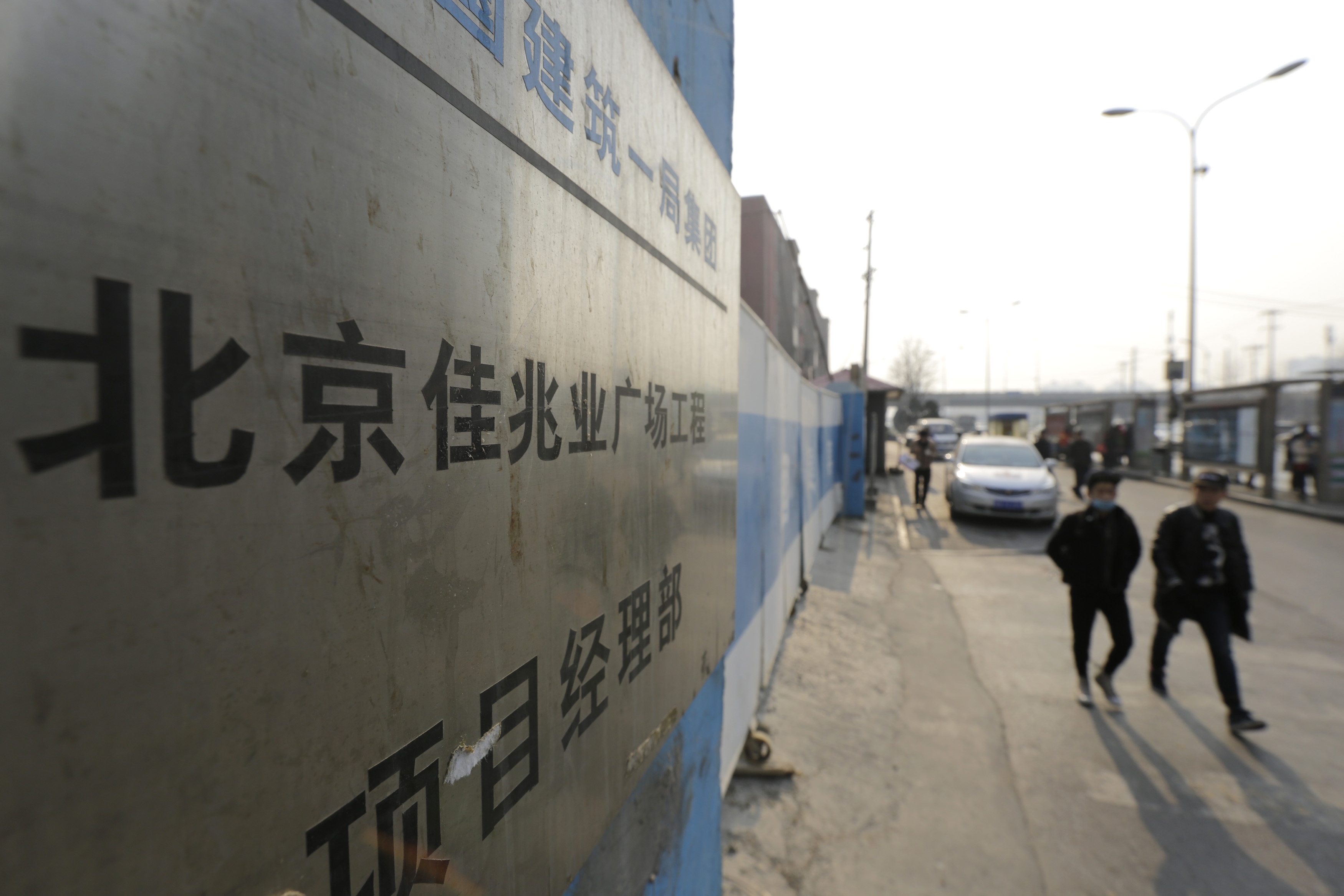 People walk past a construction site of Kaisa Plaza in Beijing