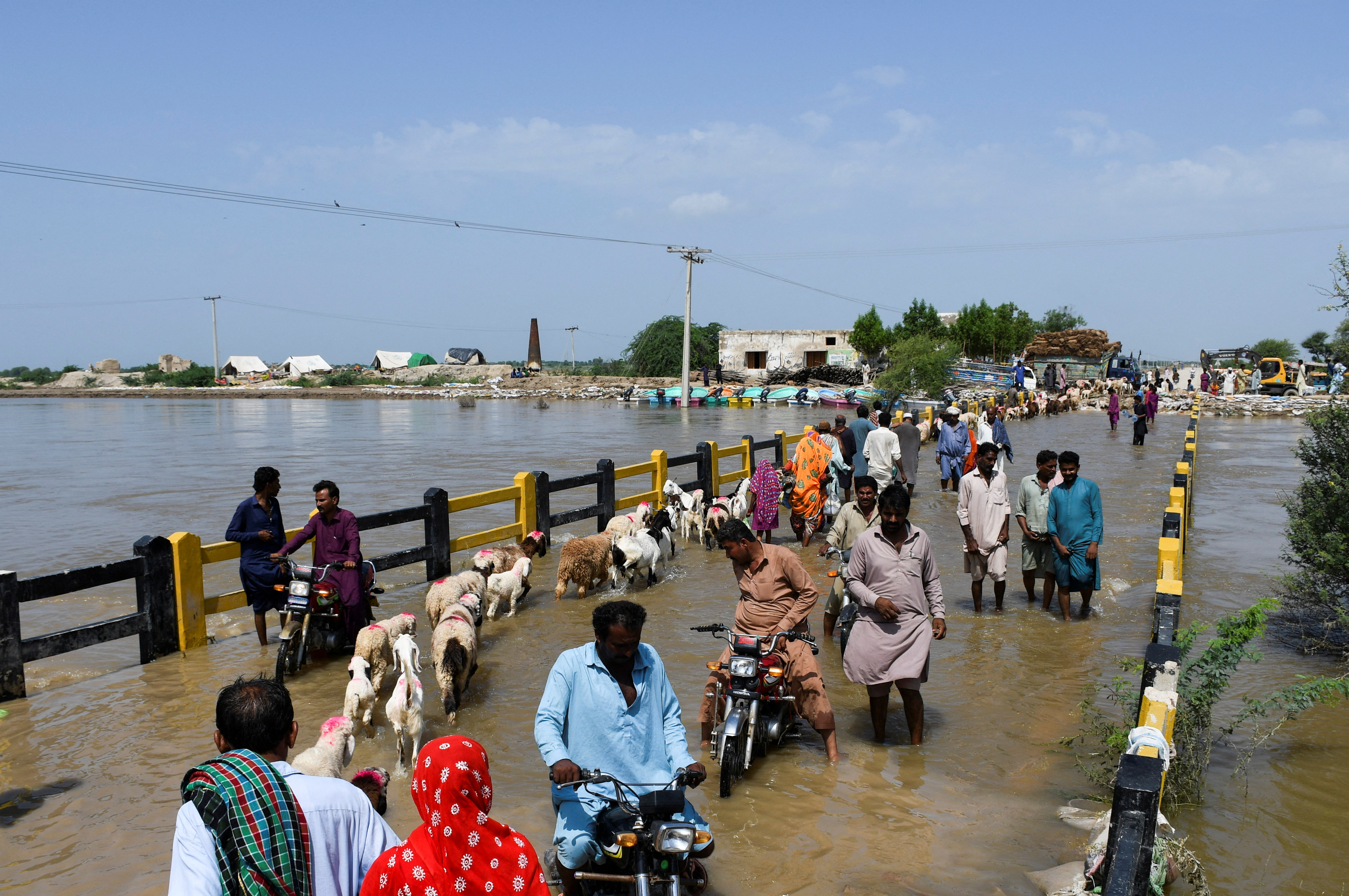 People cross a bridge amid flood waters, following rains and floods during the monsoon season in Puran Dhoro, Badin