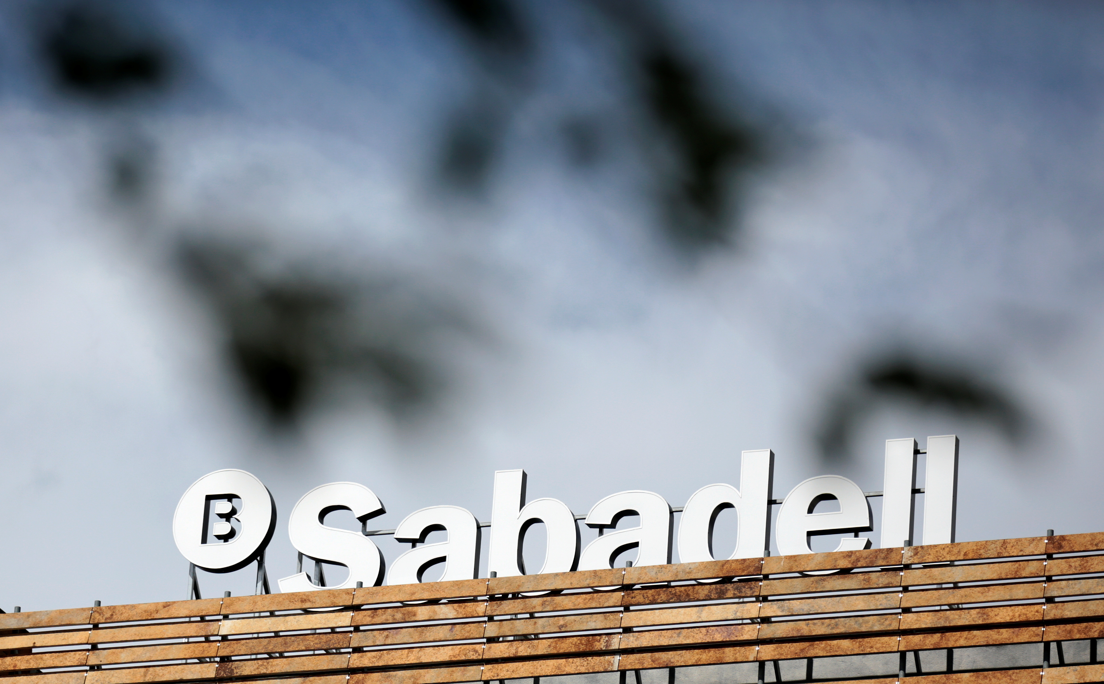 The Banco Sabadell logo can be seen behind leaves on top of a building outside Madrid, Spain
