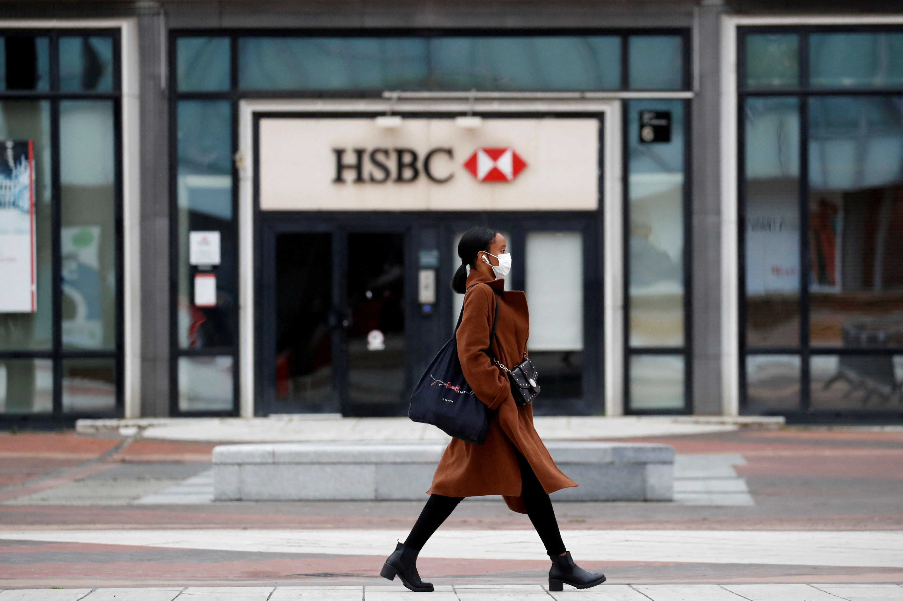 A woman wearing a protective face mask walks past a logo of HSBC bank at the financial and business district of La Defense near Paris