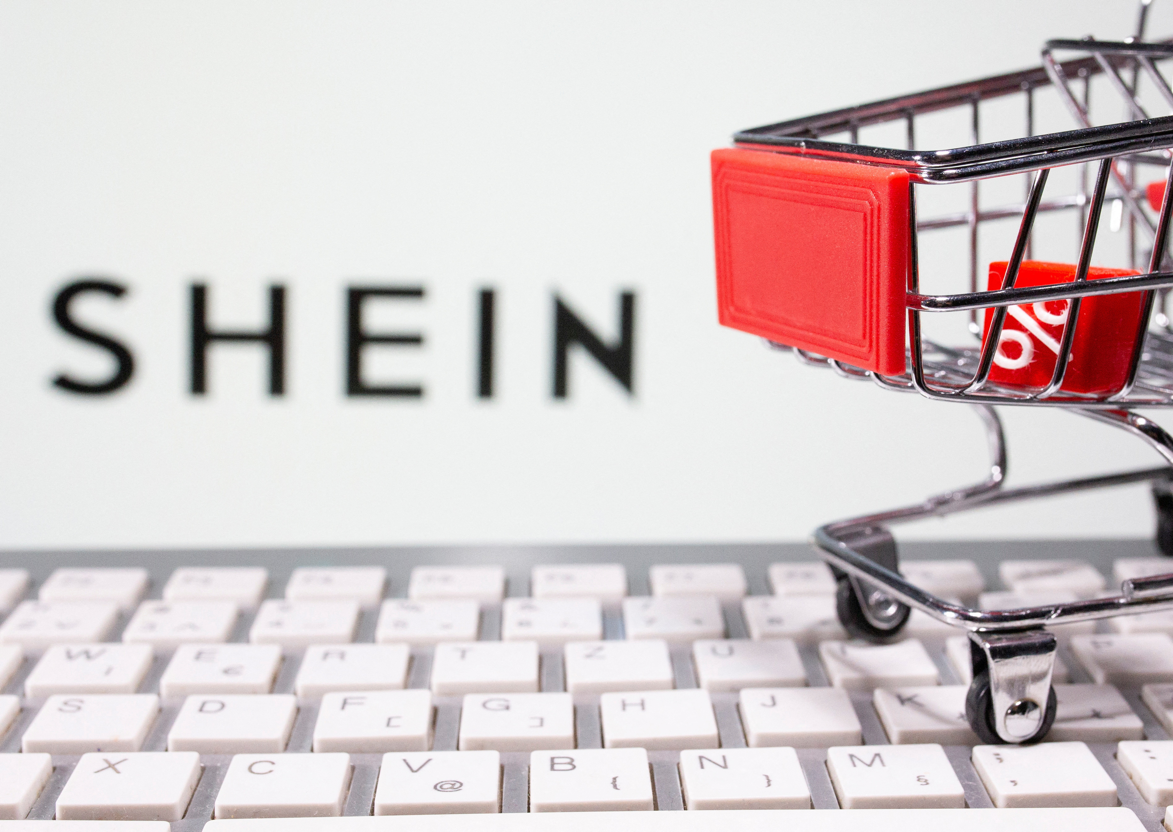 A keyboard and a shopping cart are seen in front of a displayed Shein logo in this illustration picture