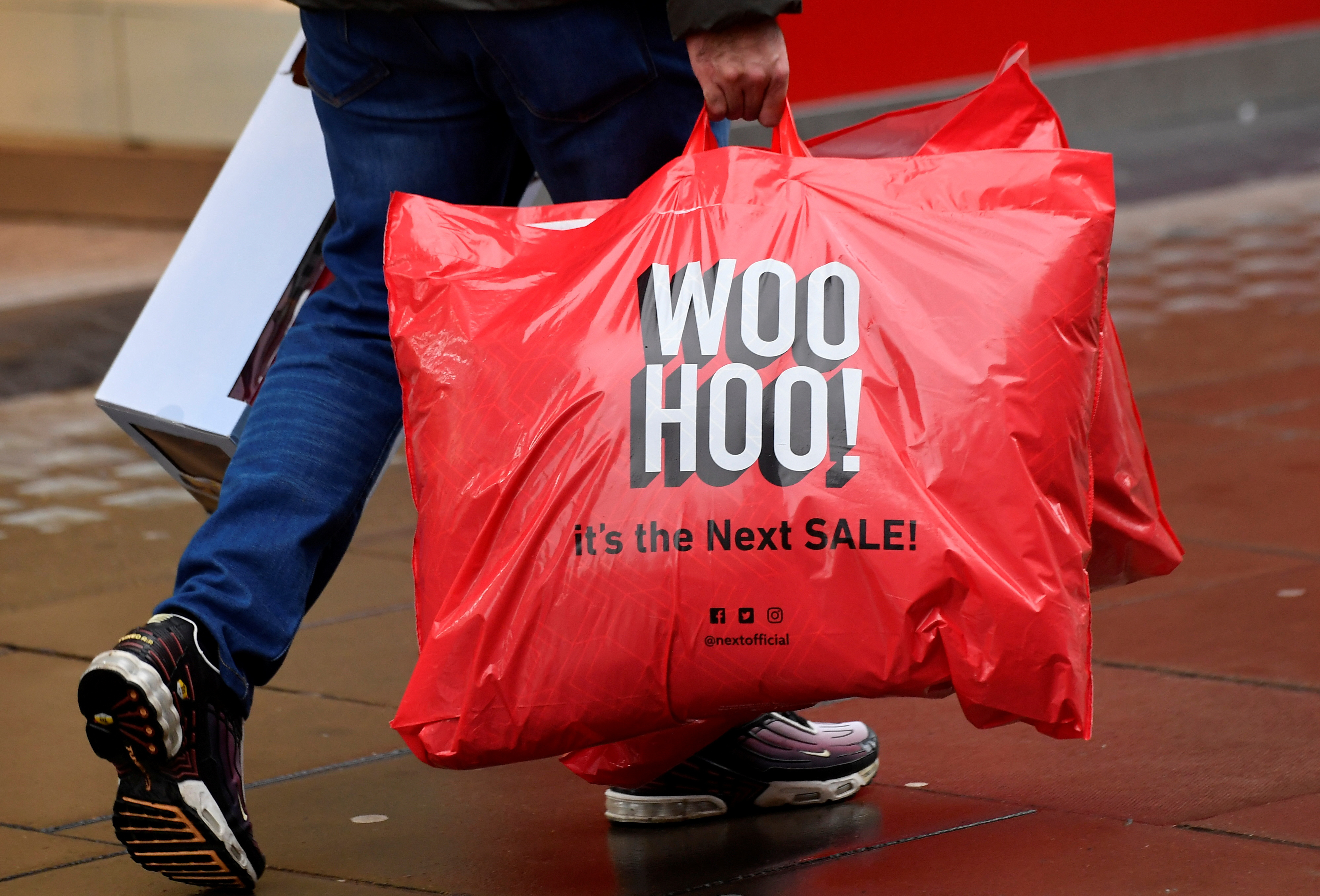 A shopper carries a bag advertising the clothing retailer Next in London