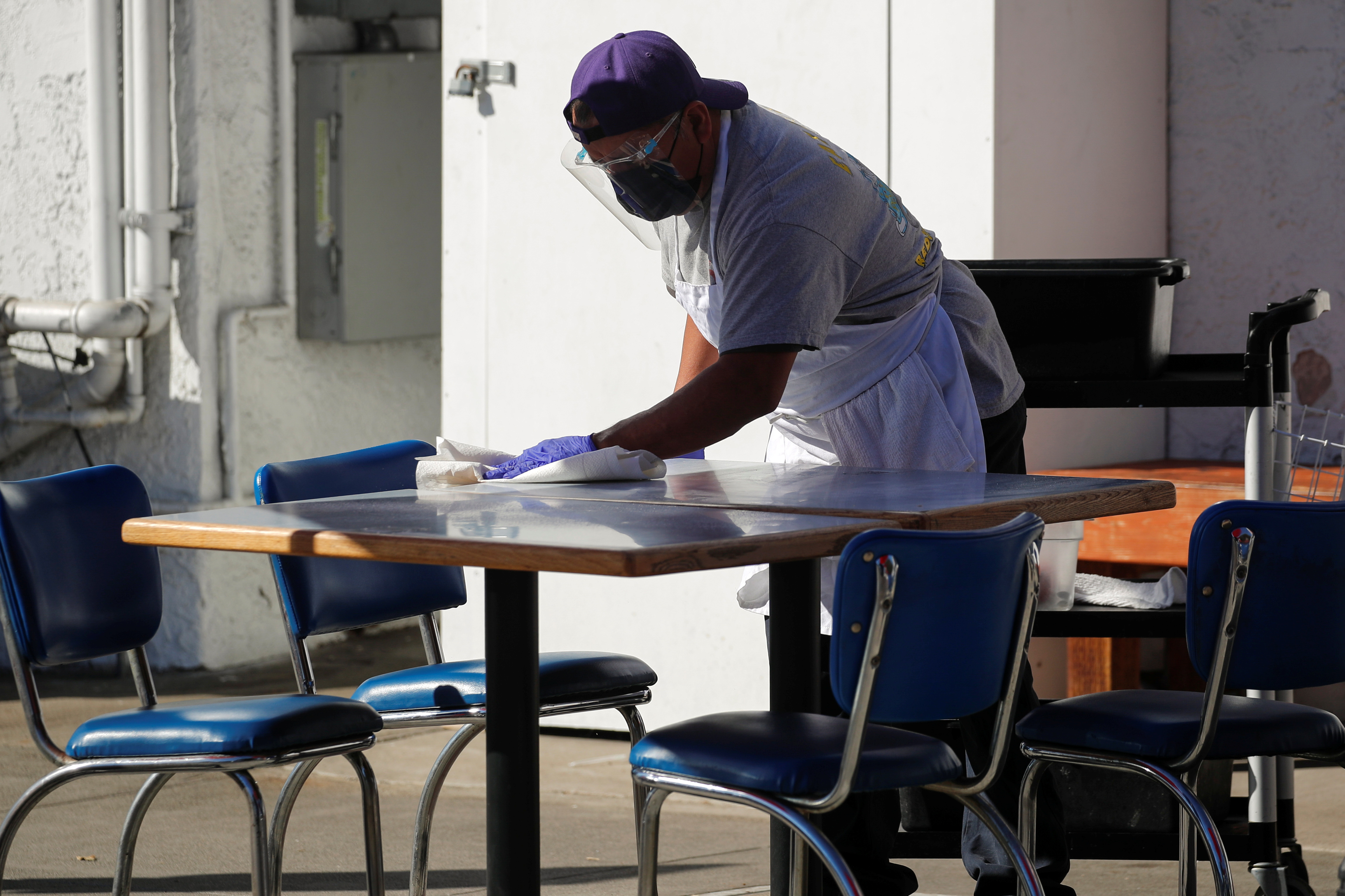 A worker clears and cleans a table along the sidewalk outside 
