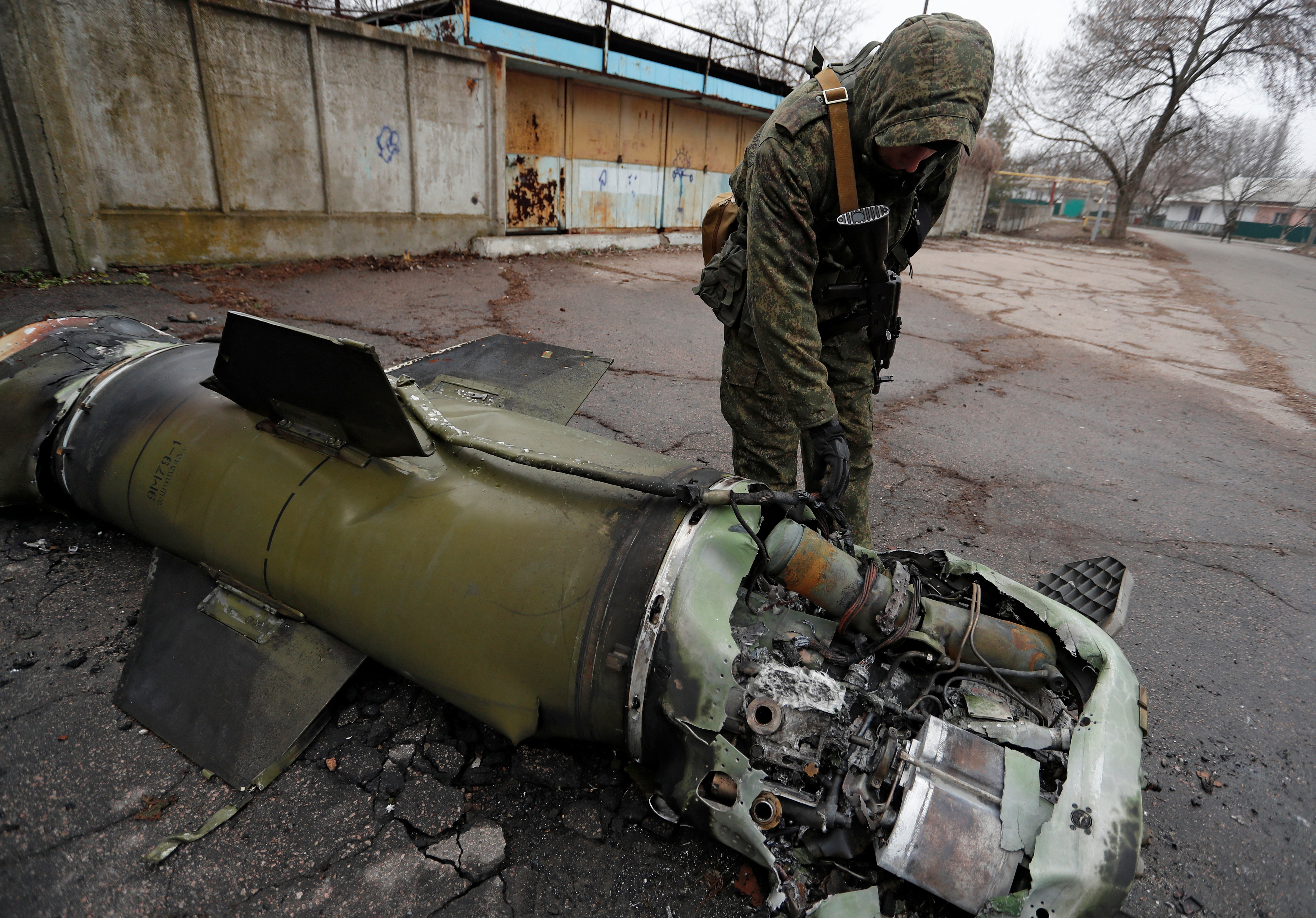 A militant of the self-proclaimed Donetsk People's Republic inspects the remains of a missile that landed on a street in Donetsk