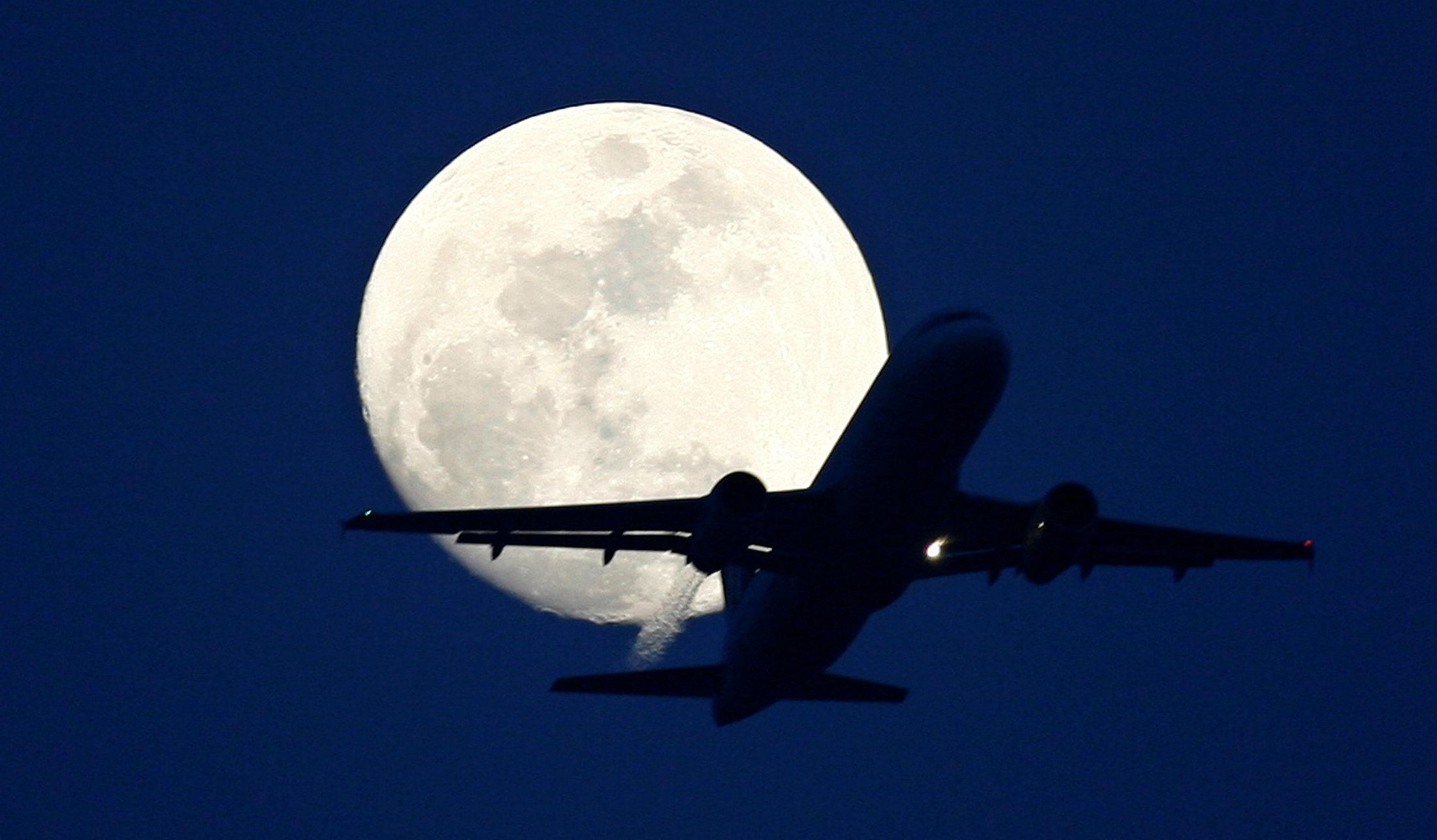 A passenger aircraft is silhouetted against the rising moon in New Delhi