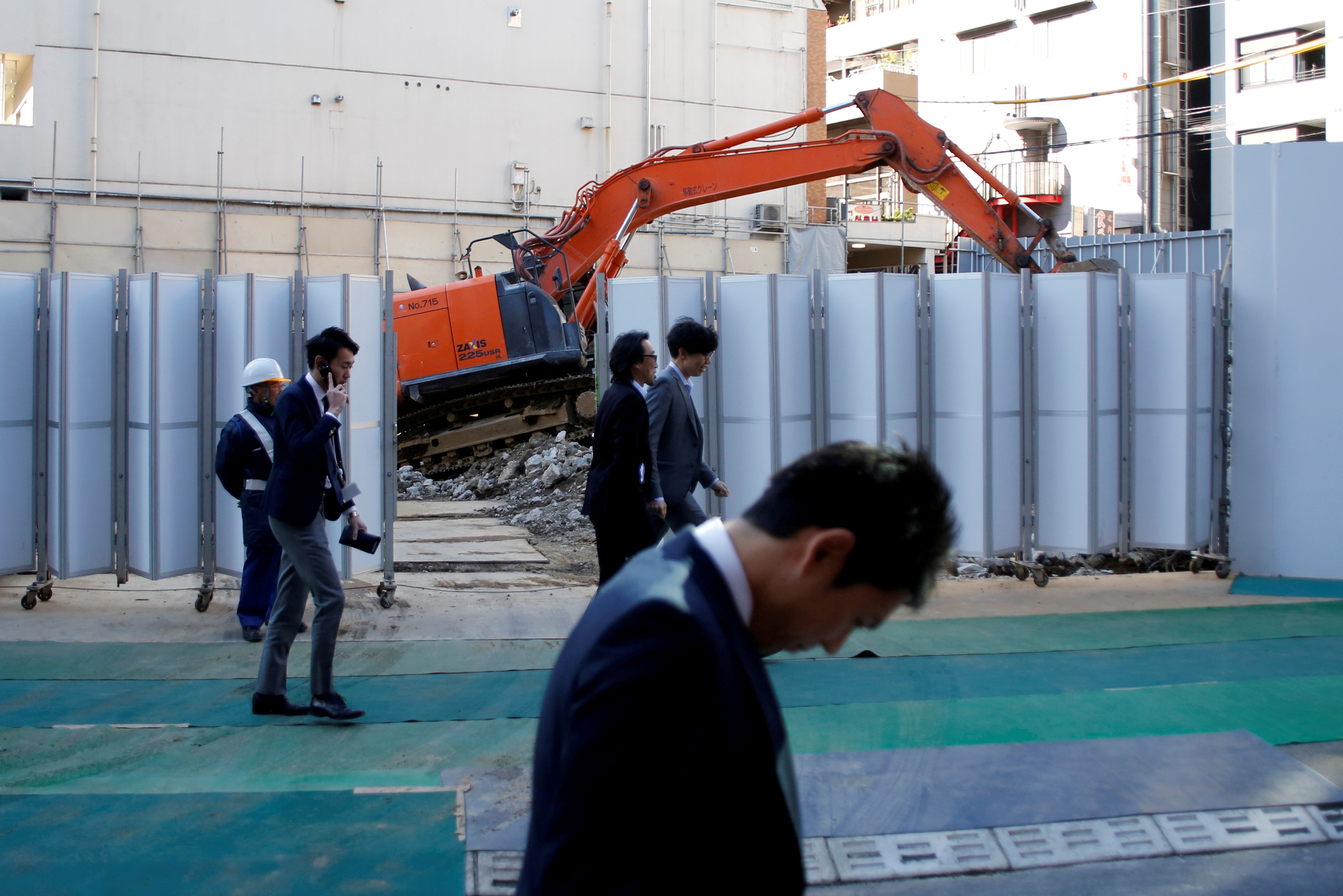 Businessmen walk past heavy machinery at a construction site in Tokyo's business district