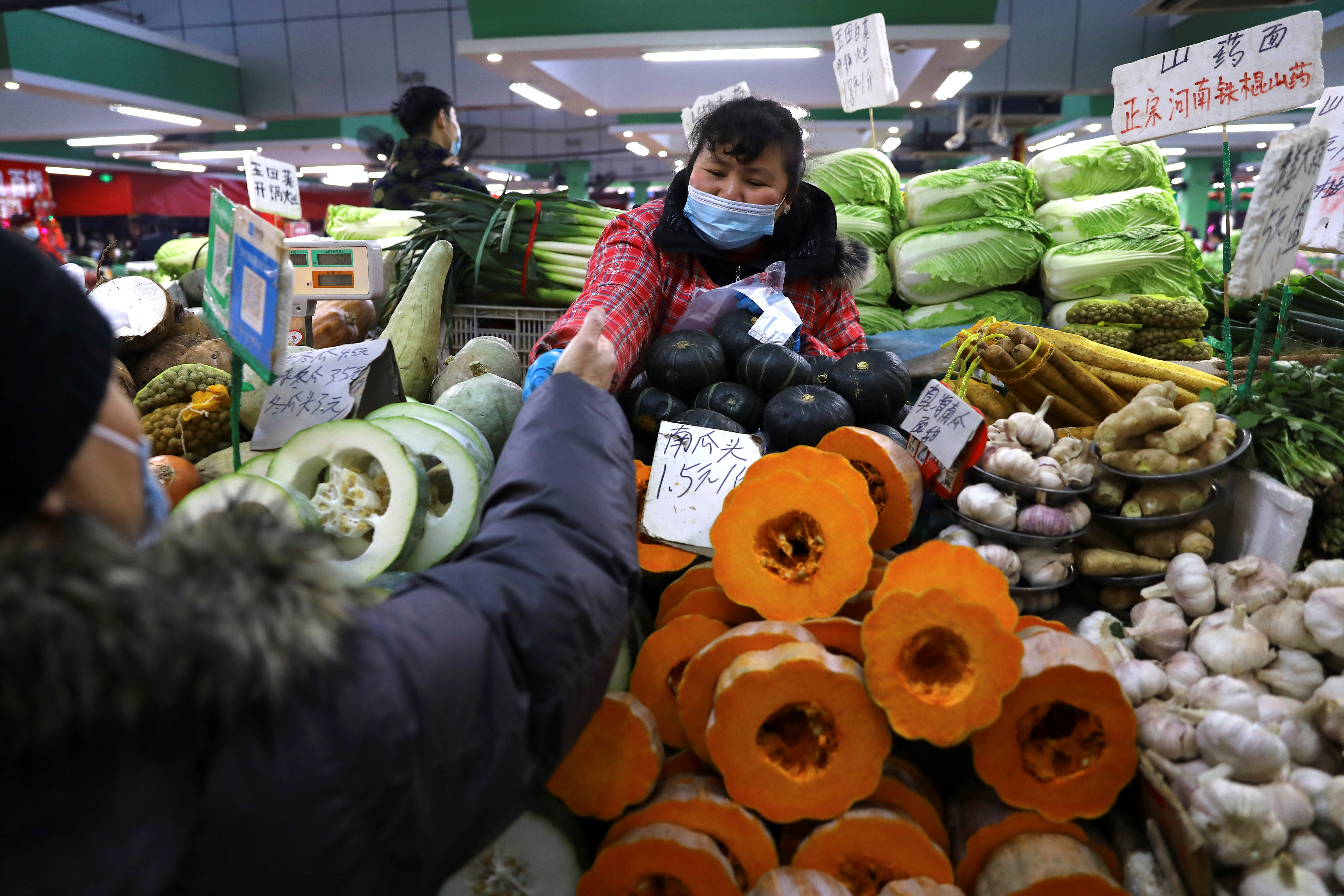 A customer buys vegetables at a stall inside a morning market in Beijing