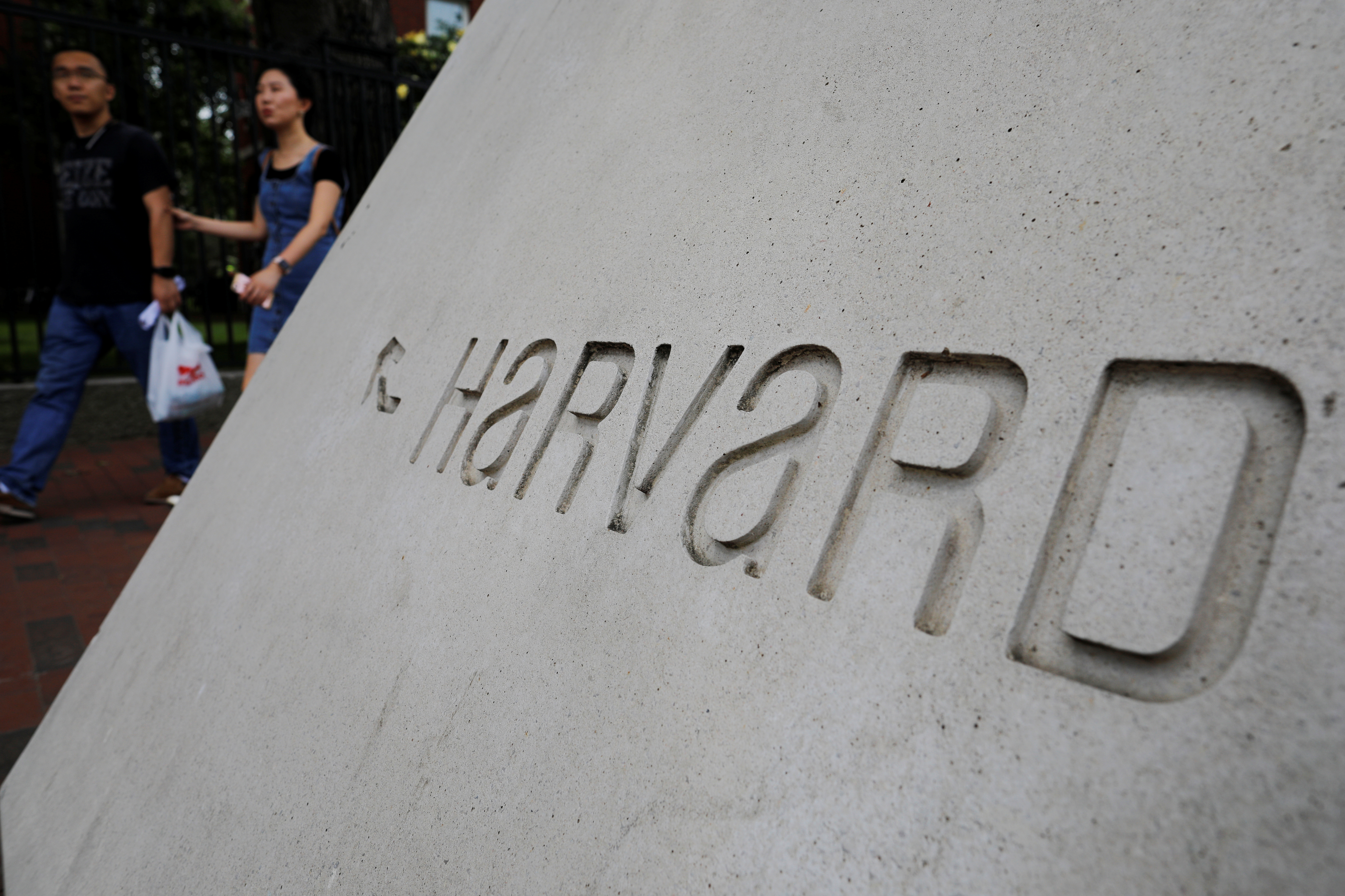 Pedestrians walk past a sign for Harvard Square outside Harvard University in Cambridge