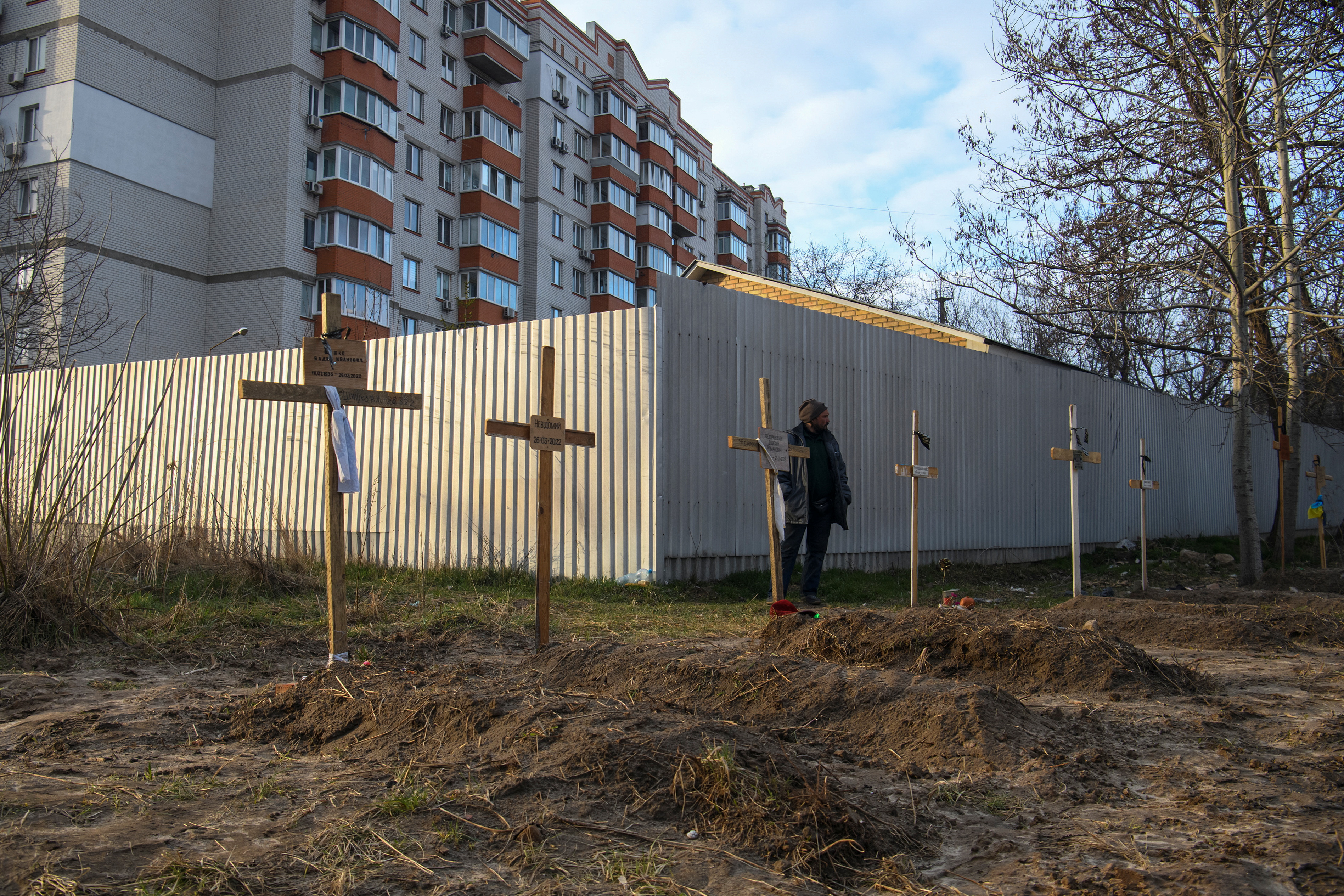 A man stands next to graves with bodies of civilians, who according to local residents were killed by Russian soldiers, in Bucha