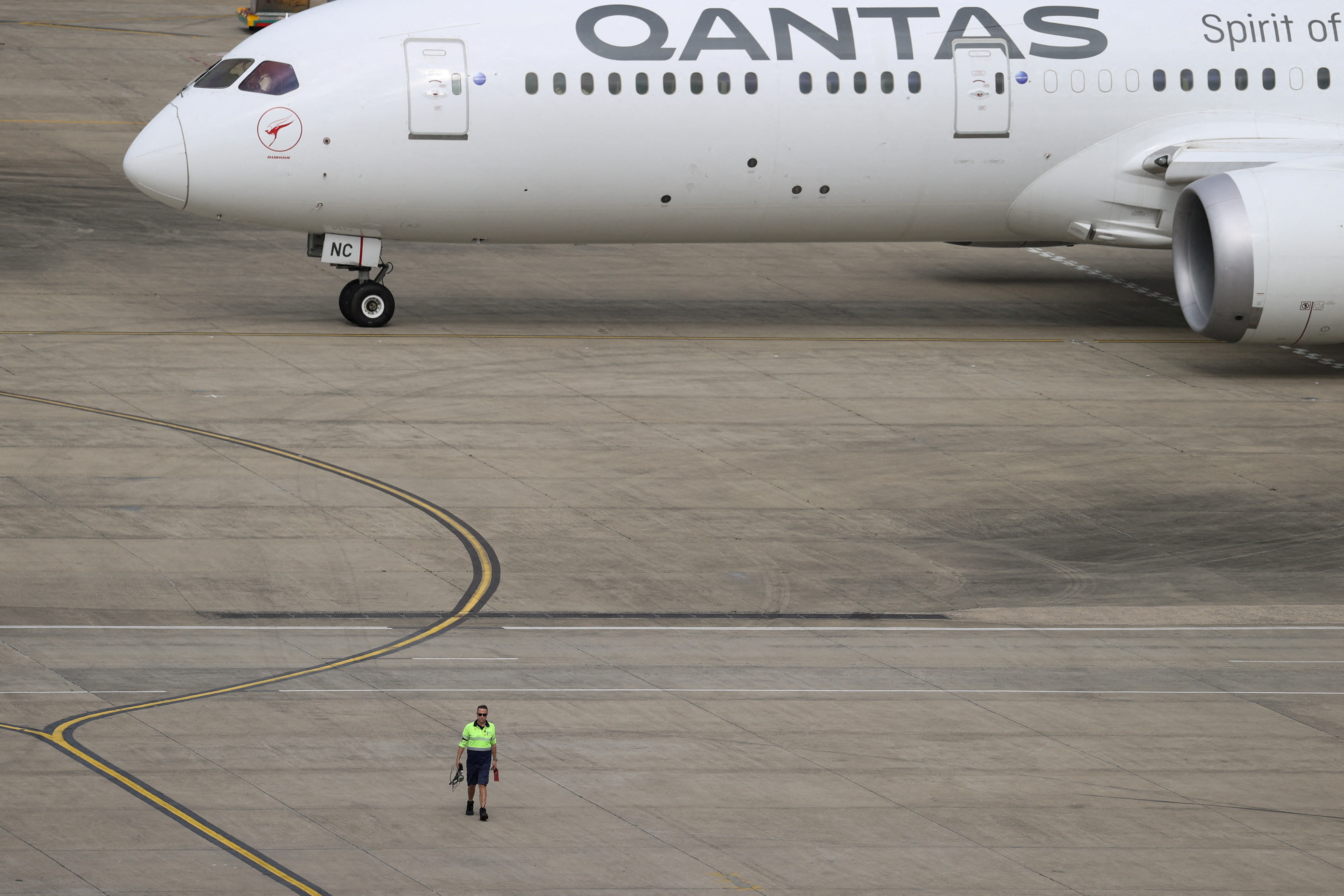 A ground worker walking near a Qantas plane is seen from the international terminal at Sydney Airport