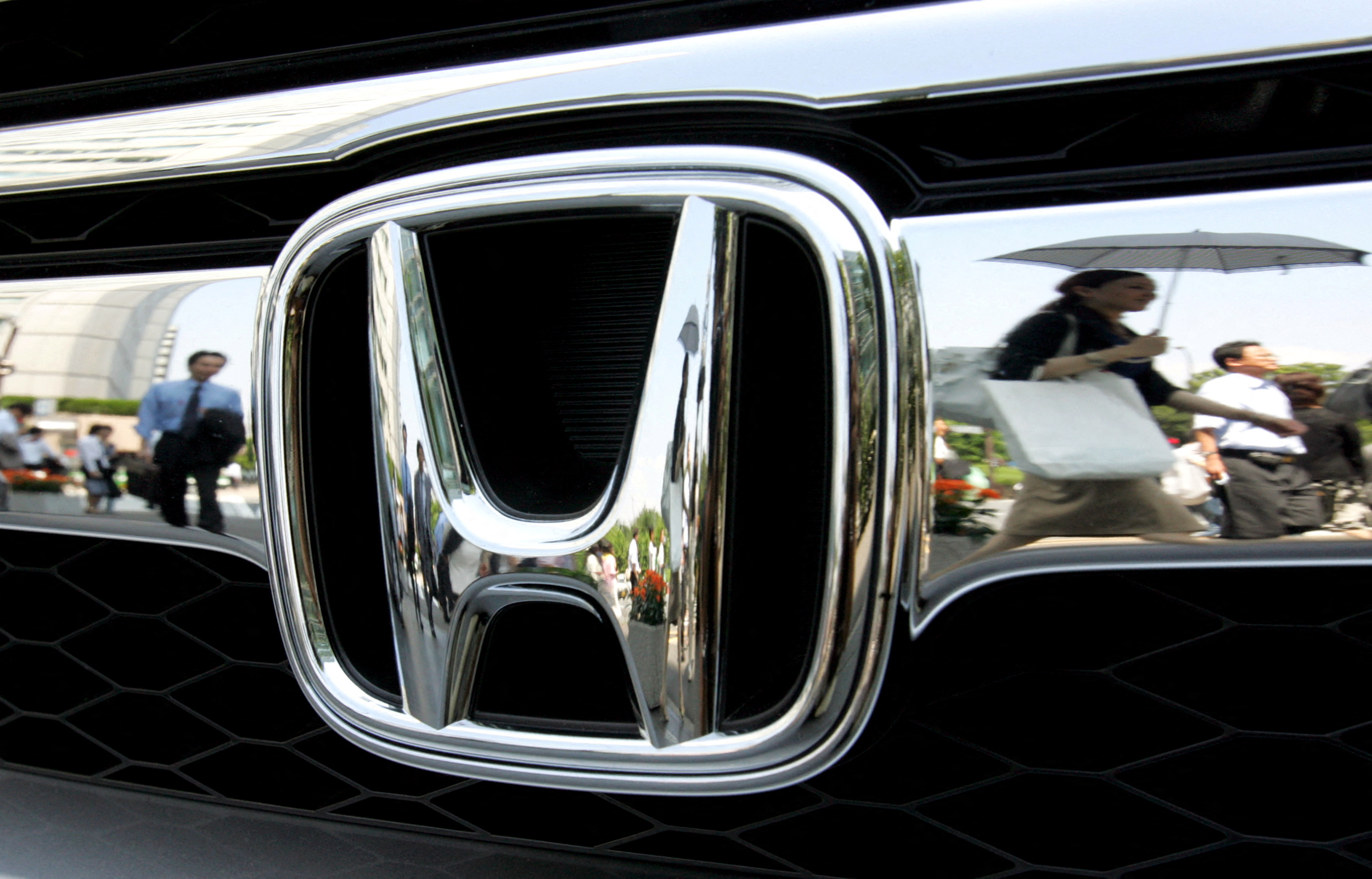 Pedestrians are reflected on Honda Motor Co. badge outside company headquarters in Tokyo
