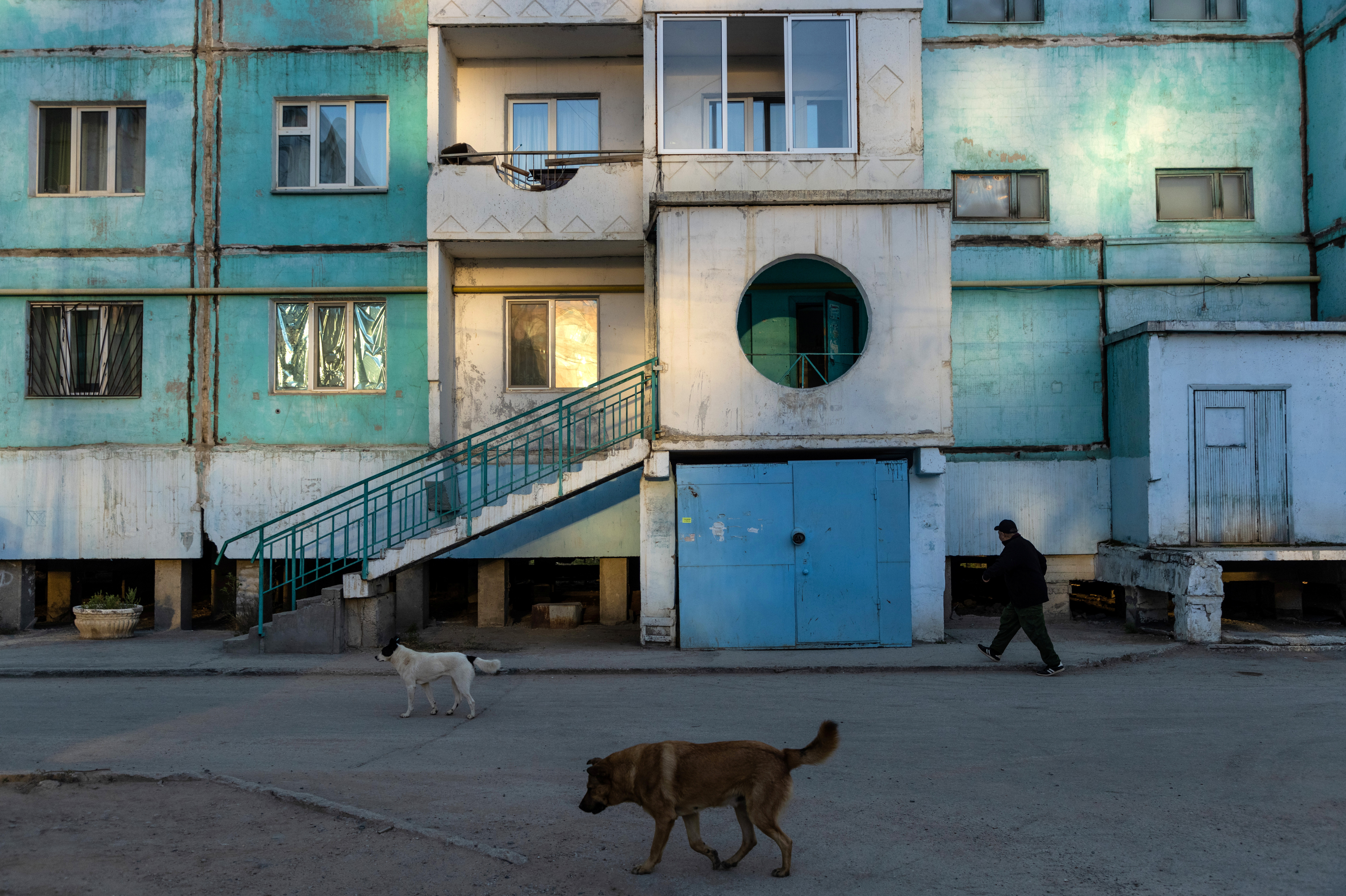 A man and stray dogs pass by a residential block constructed on stilts early morning in Yakutsk