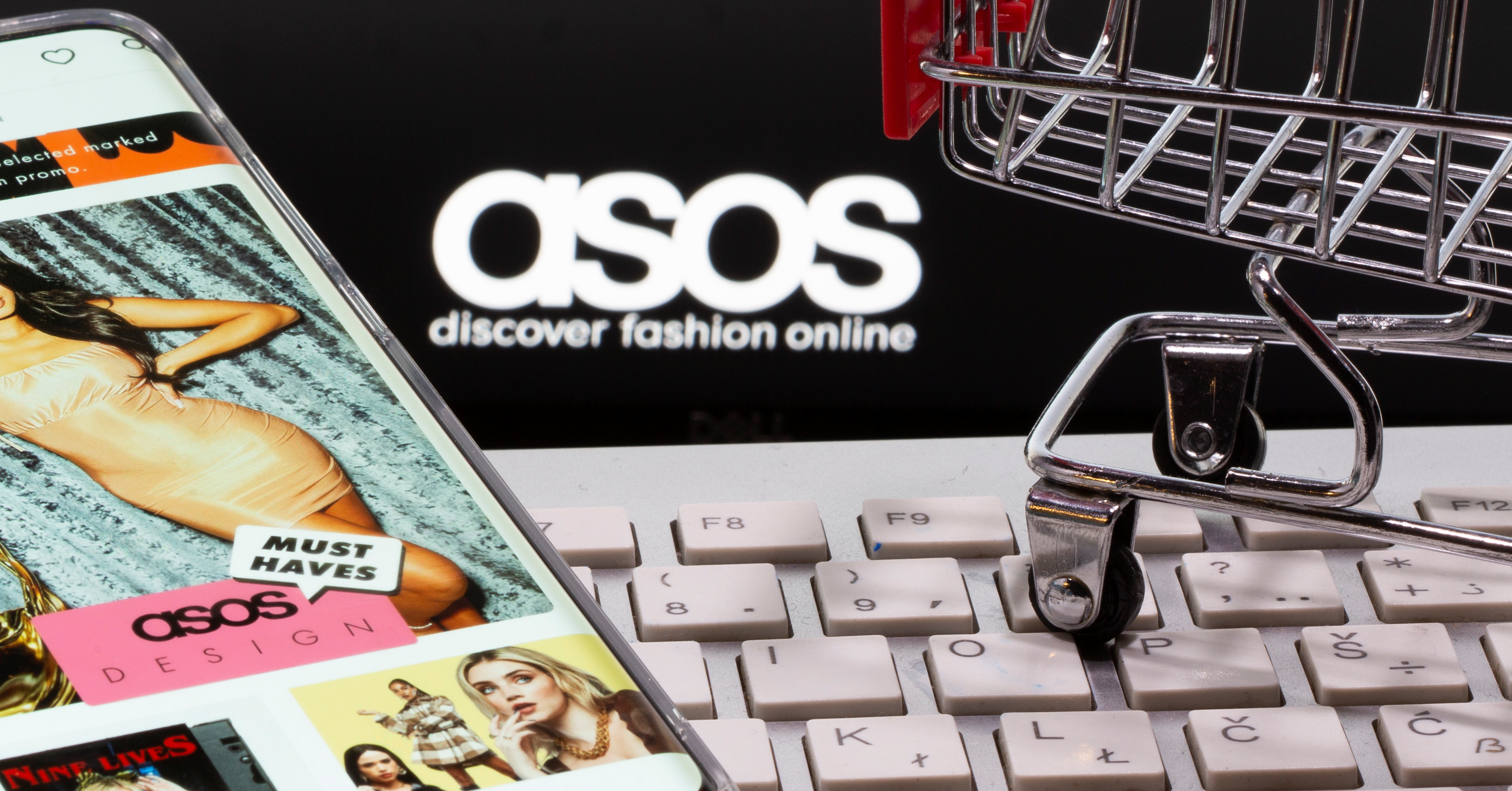 Smartphone with ASOS app, a keyboard and a shopping cart are seen in front of a displayed ASOS logo in this illustration picture