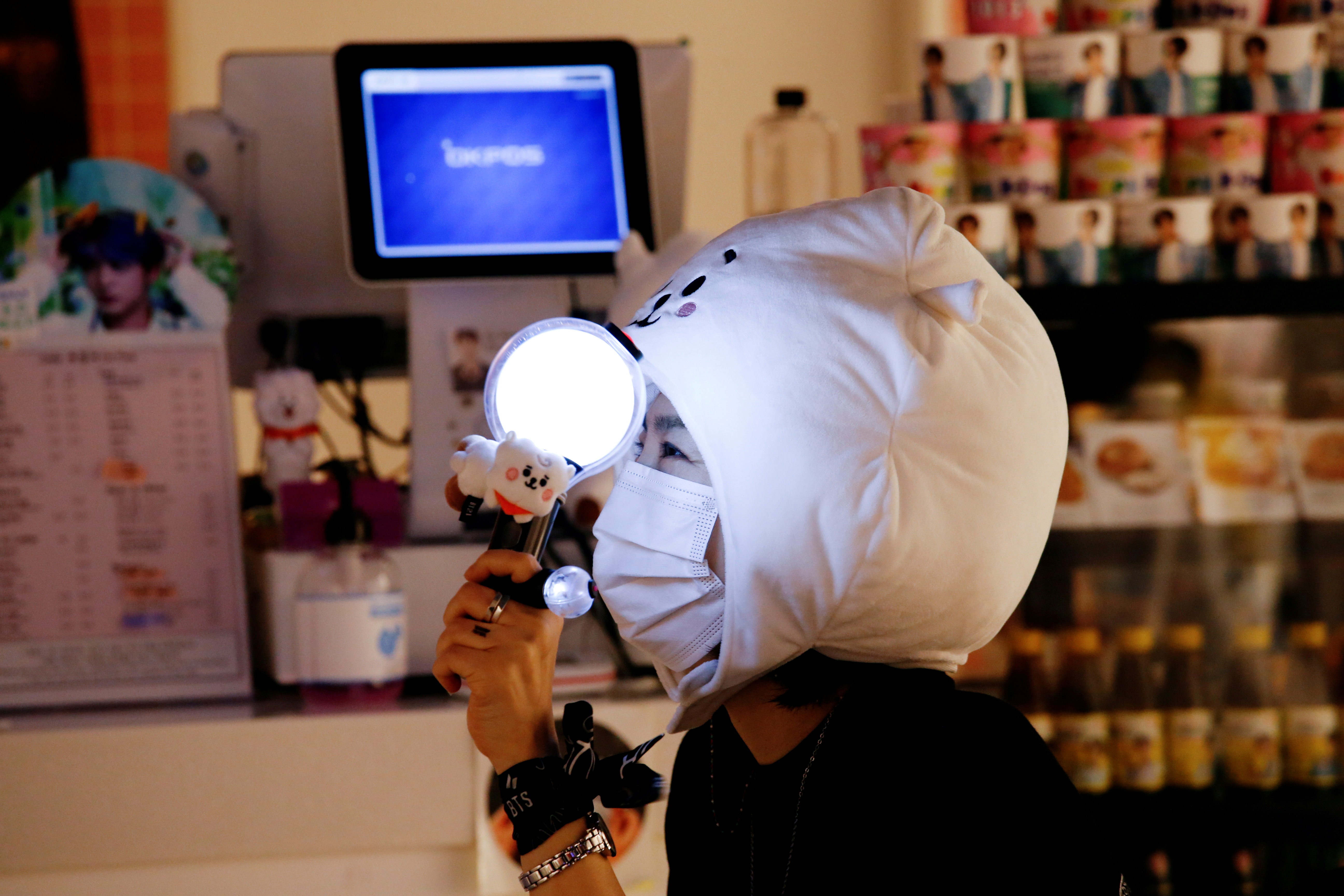 A fan of K-pop idol boy band BTS watches a live streaming online concert, wearing a protective mask at a cafe, in Seoul