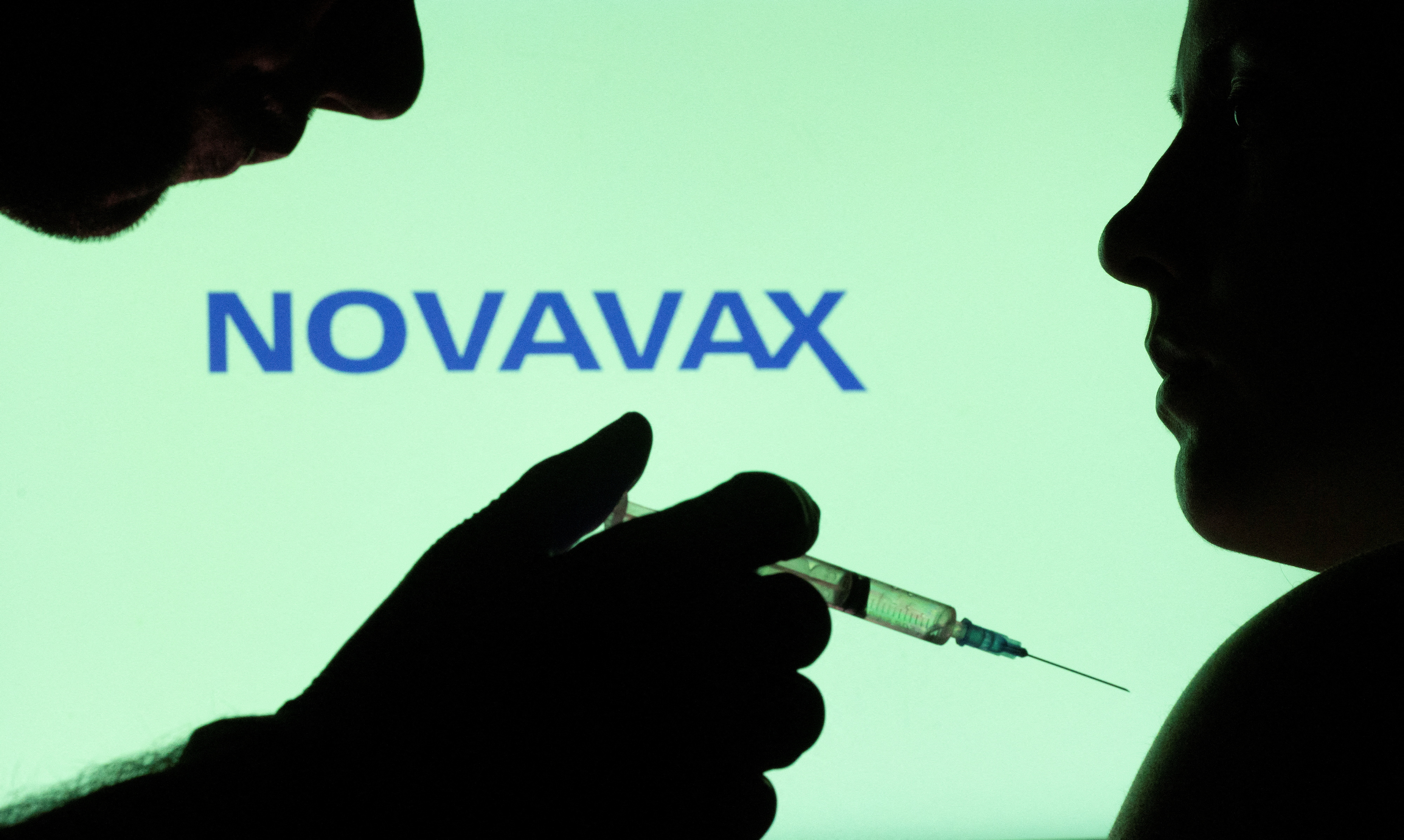 People pose with syringe with needle in front of displayed Novavax logo