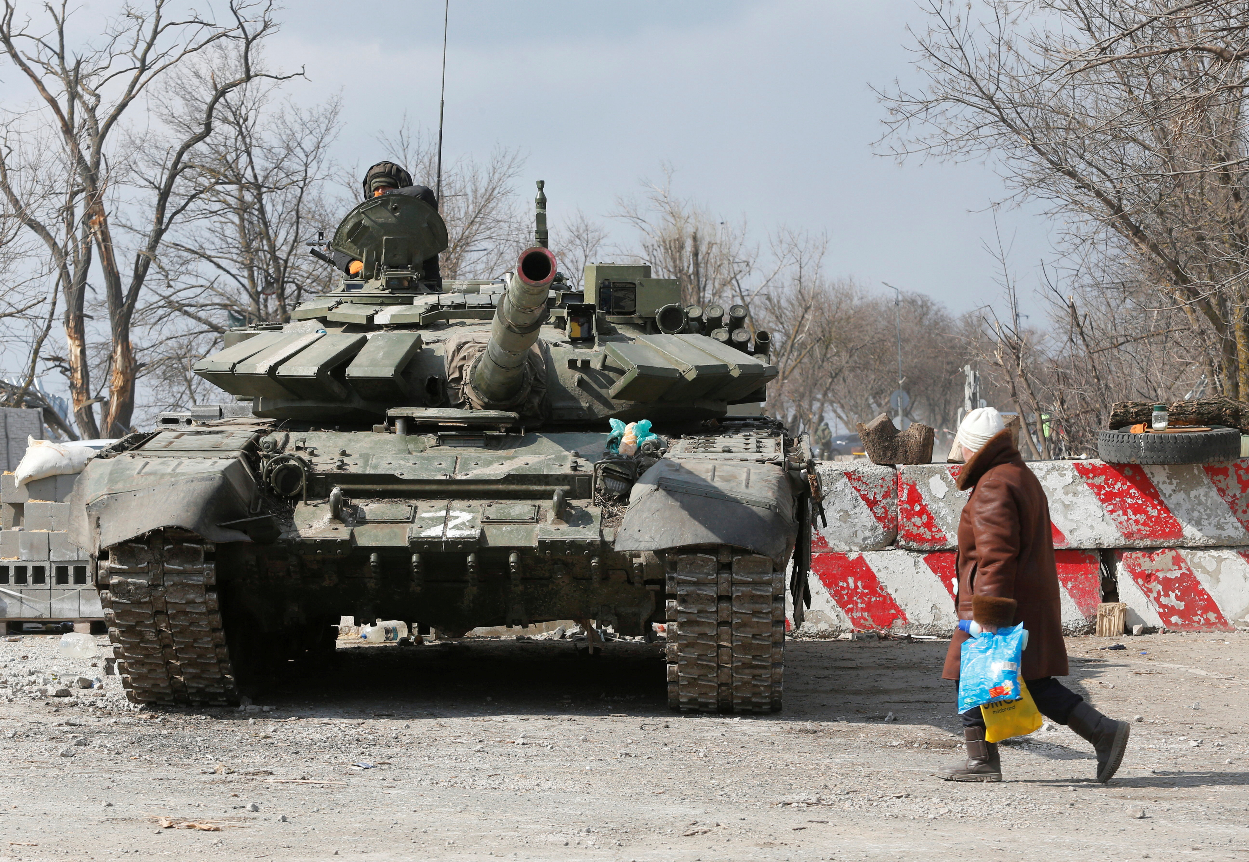 A local resident walks past a tank of pro-Russian troops in the besieged city of Mariupol