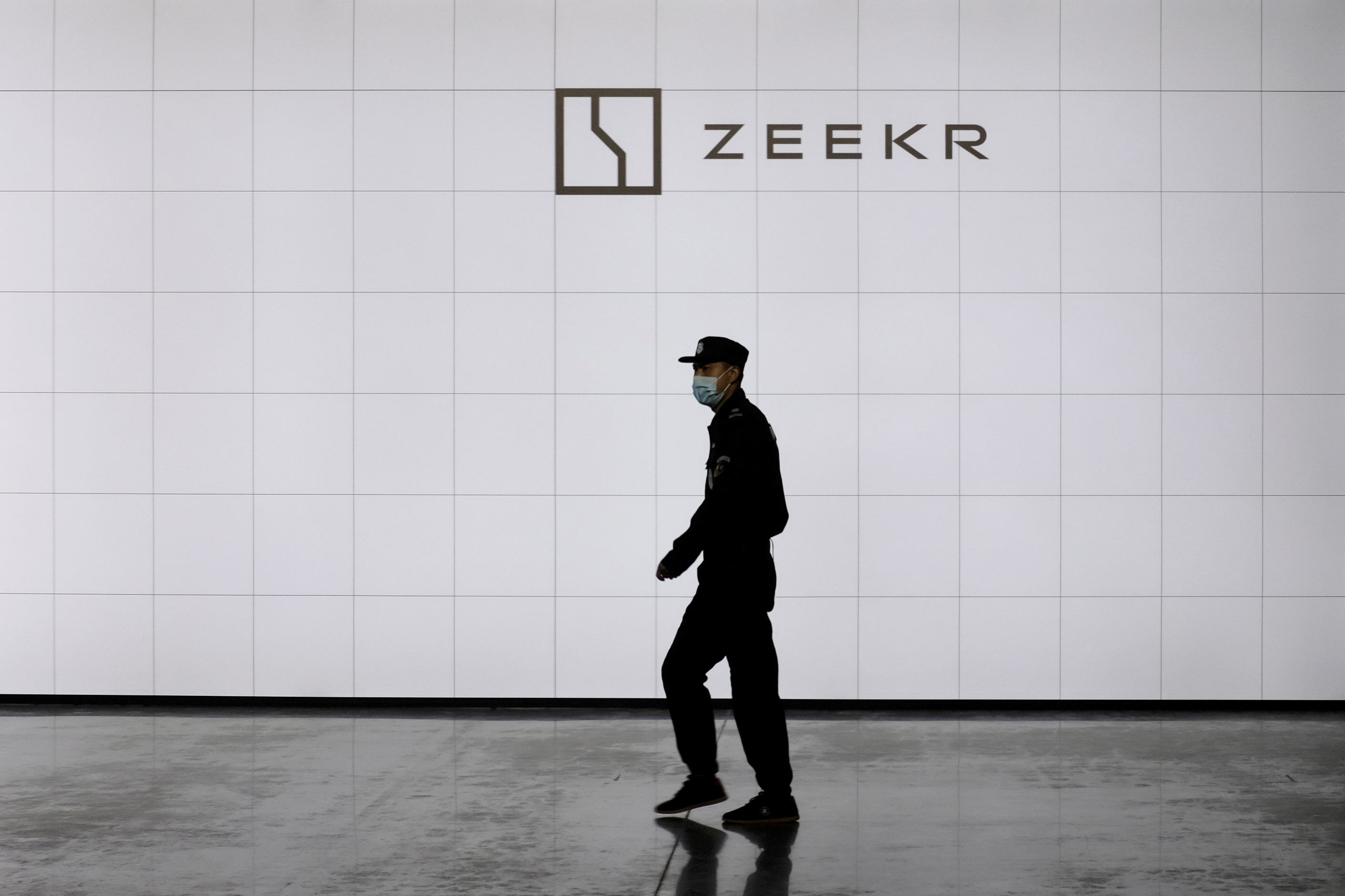 A security guard walks past a sign of Geely's new premium electric vehicle (EV) brand Zeekr at its factory in Ningbo, Zhejiang province, China April 15, 2021. REUTERS/Yilei Sun
