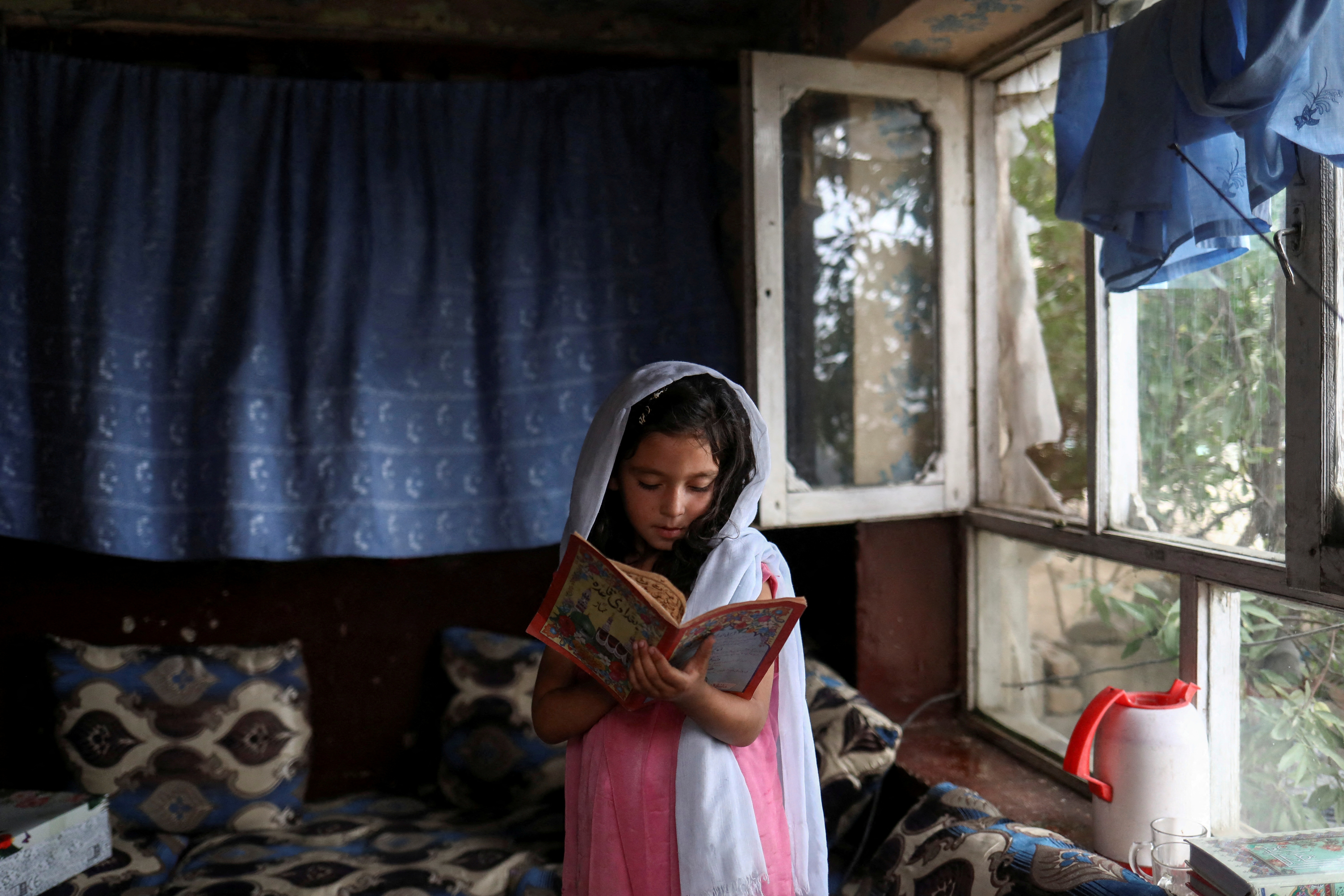 FILE PHOTO - An Afghan girl reads a book inside her home in Kabul