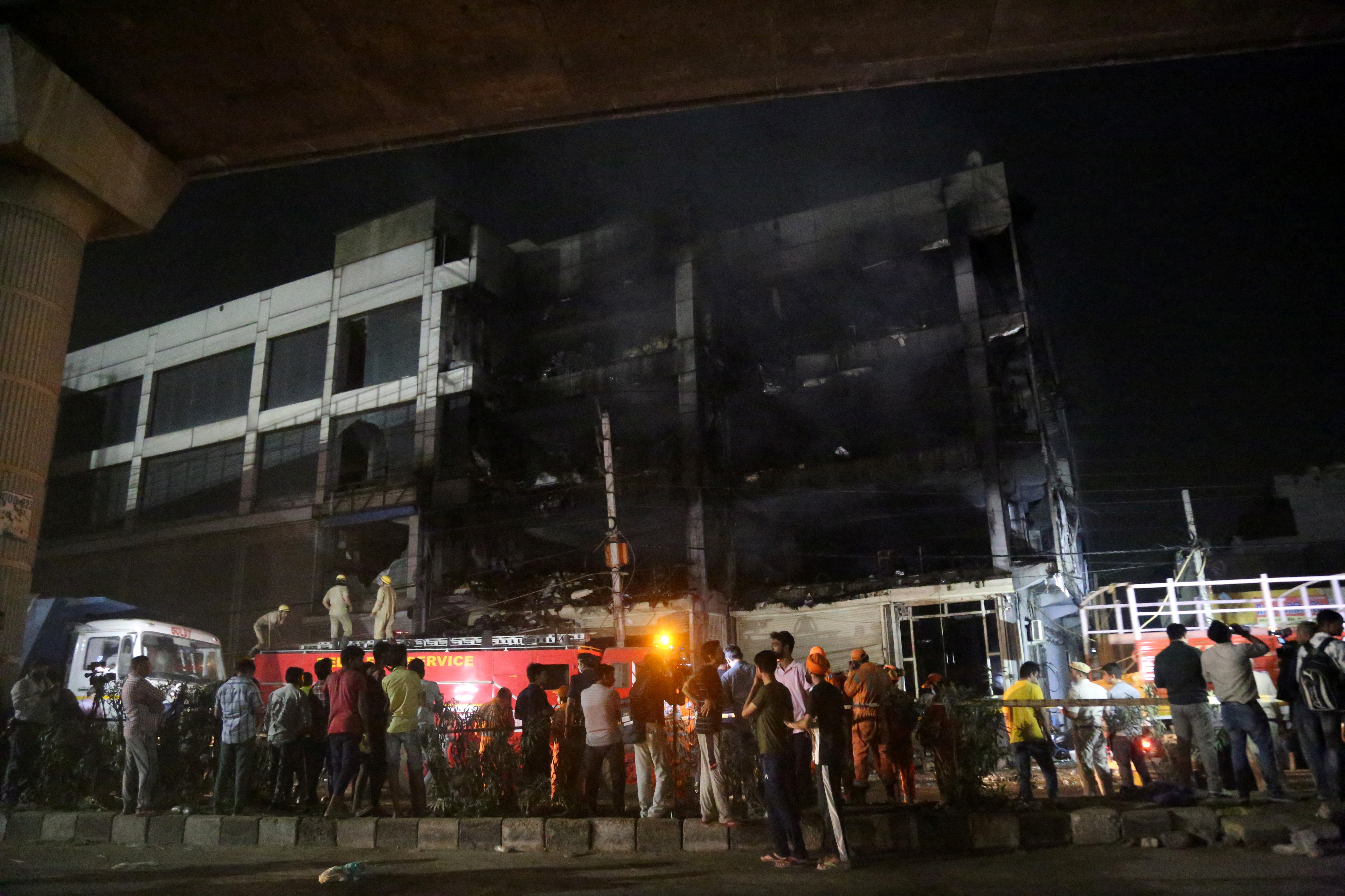 اعضای امداد و ناظران در حالی ایستاده اند که آتش نشانان آتشی را که در یک ساختمان تجاری در حومه غربی دهلی رخ داده بود خاموش می کنند.