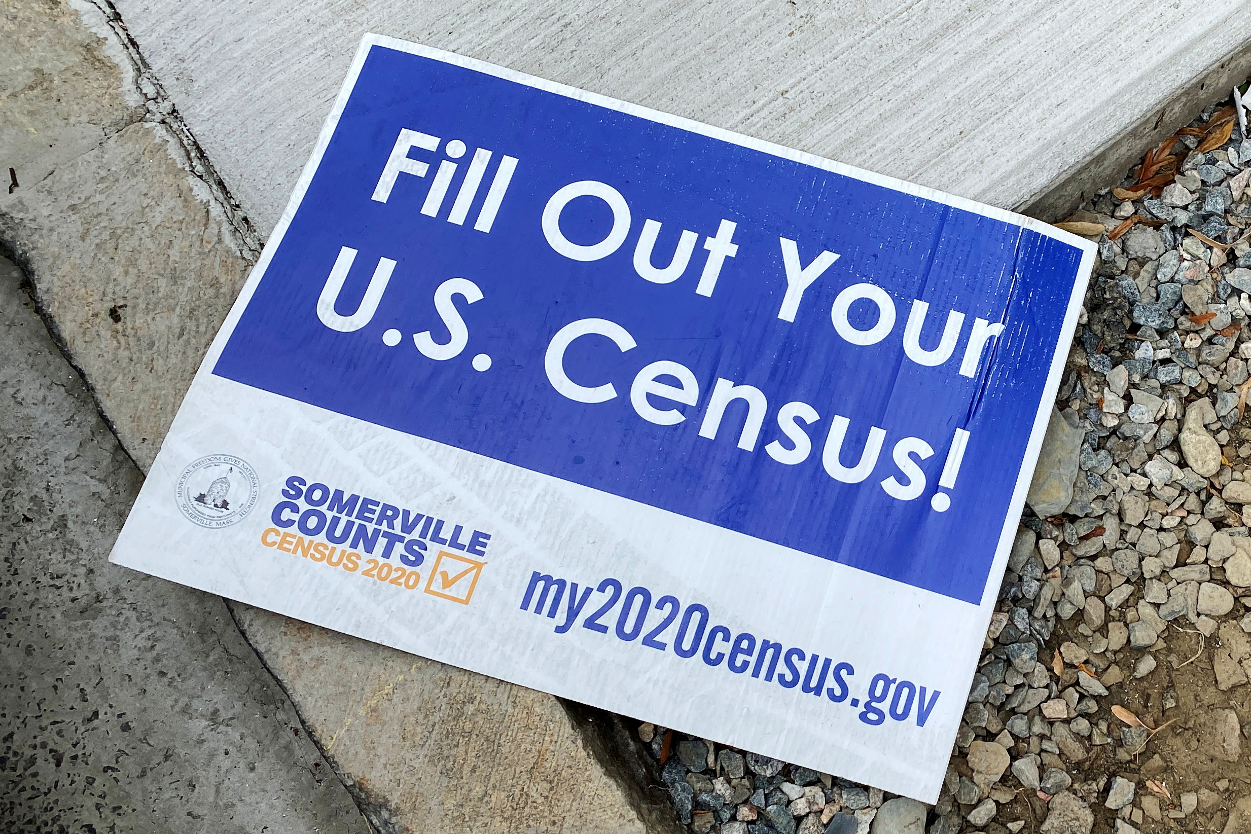 A sign encouraging participation in the U.S. Census lies on a sidewalk in Somerville