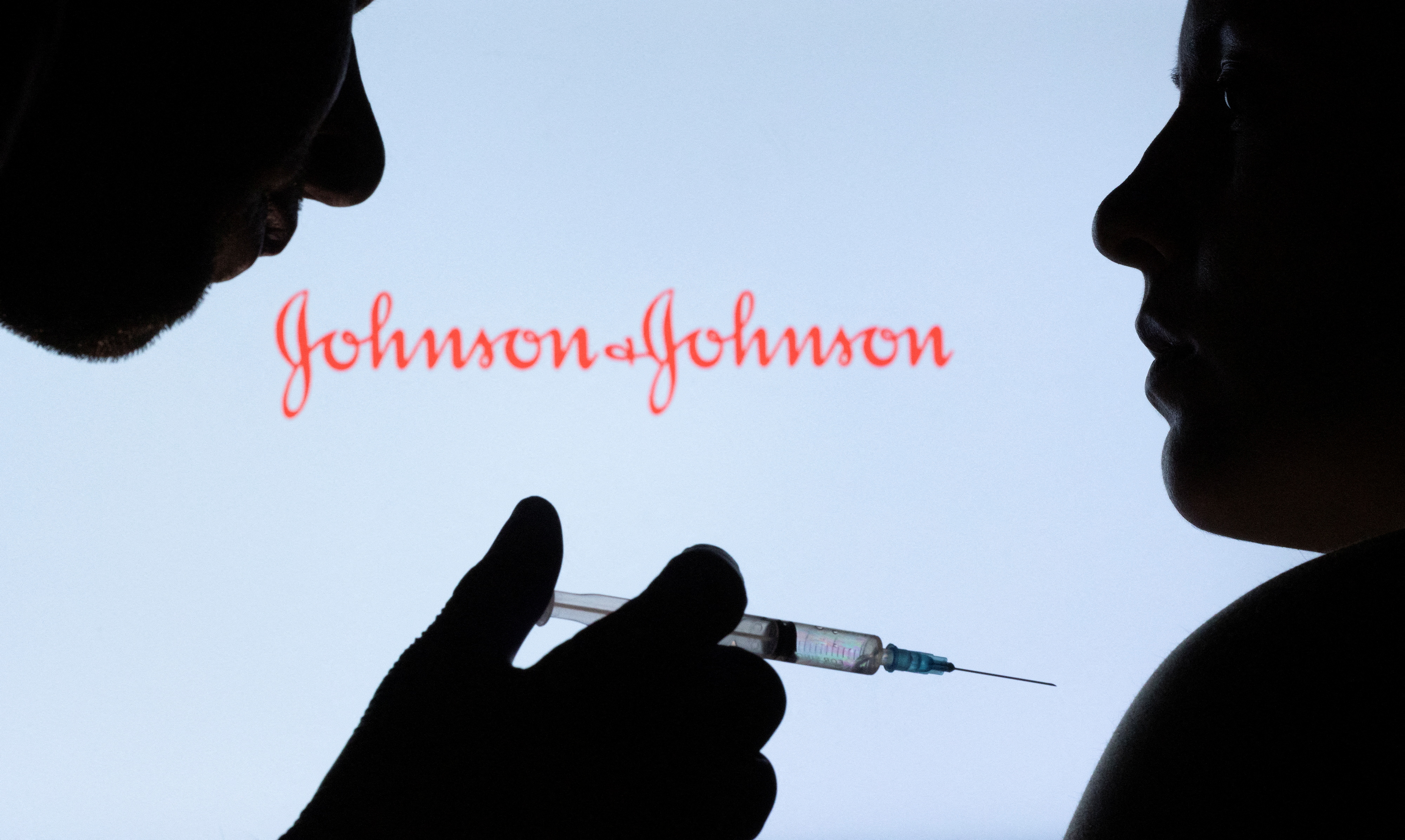 People pose with syringe with needle in front of displayed Johnson&Johnson logo