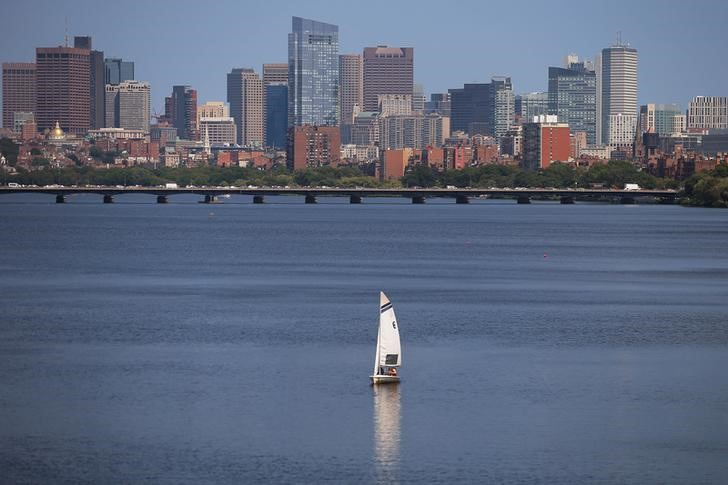 A sailboat makes its way along the Charles River in front of the skyline of Boston