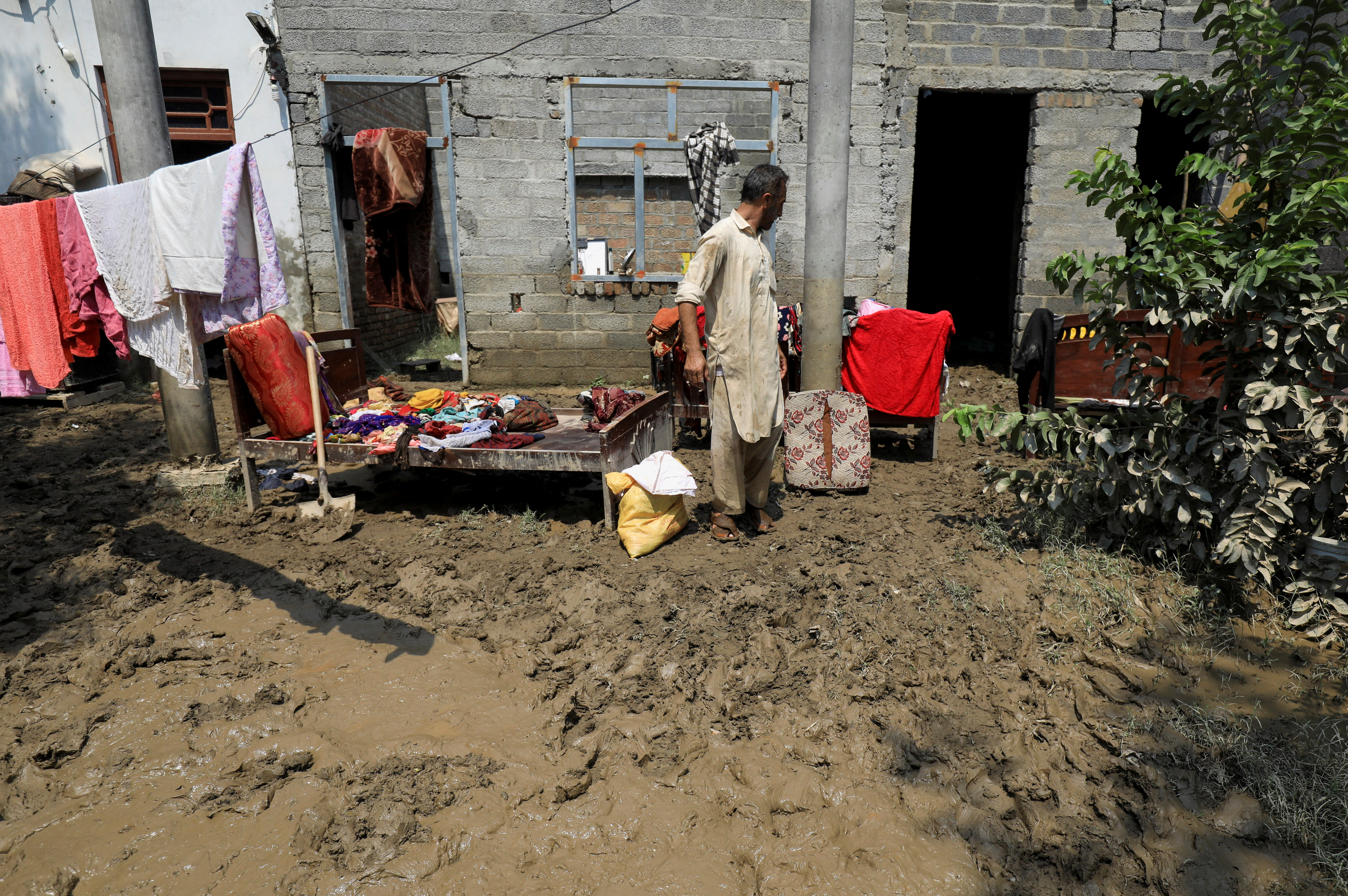 A man stands amid belongings as he clears his house, following rains and floods during the monsoon season in Charsadda,