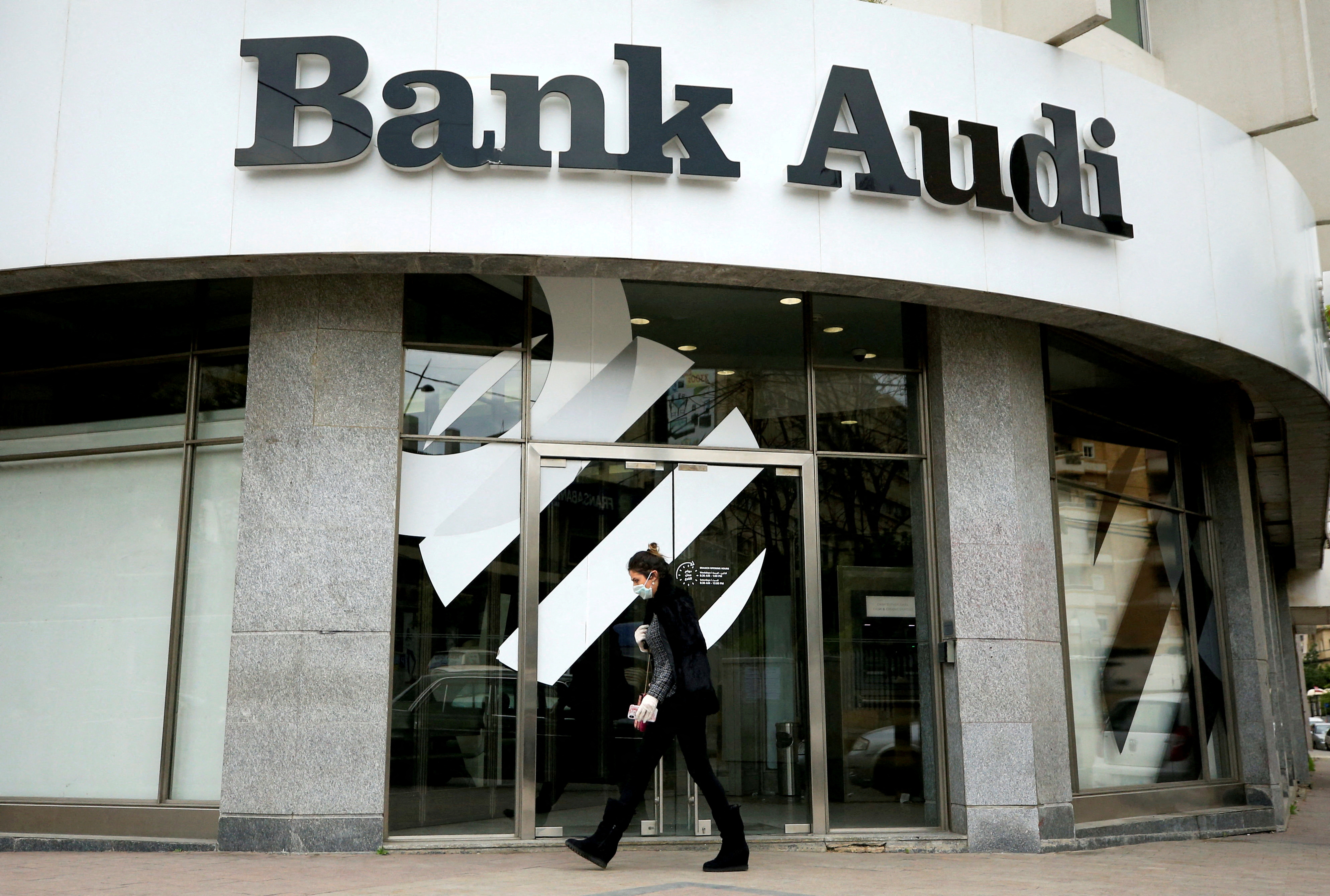 A woman wearing a face mask walks near a closed branch of Bank Audi in Sidon