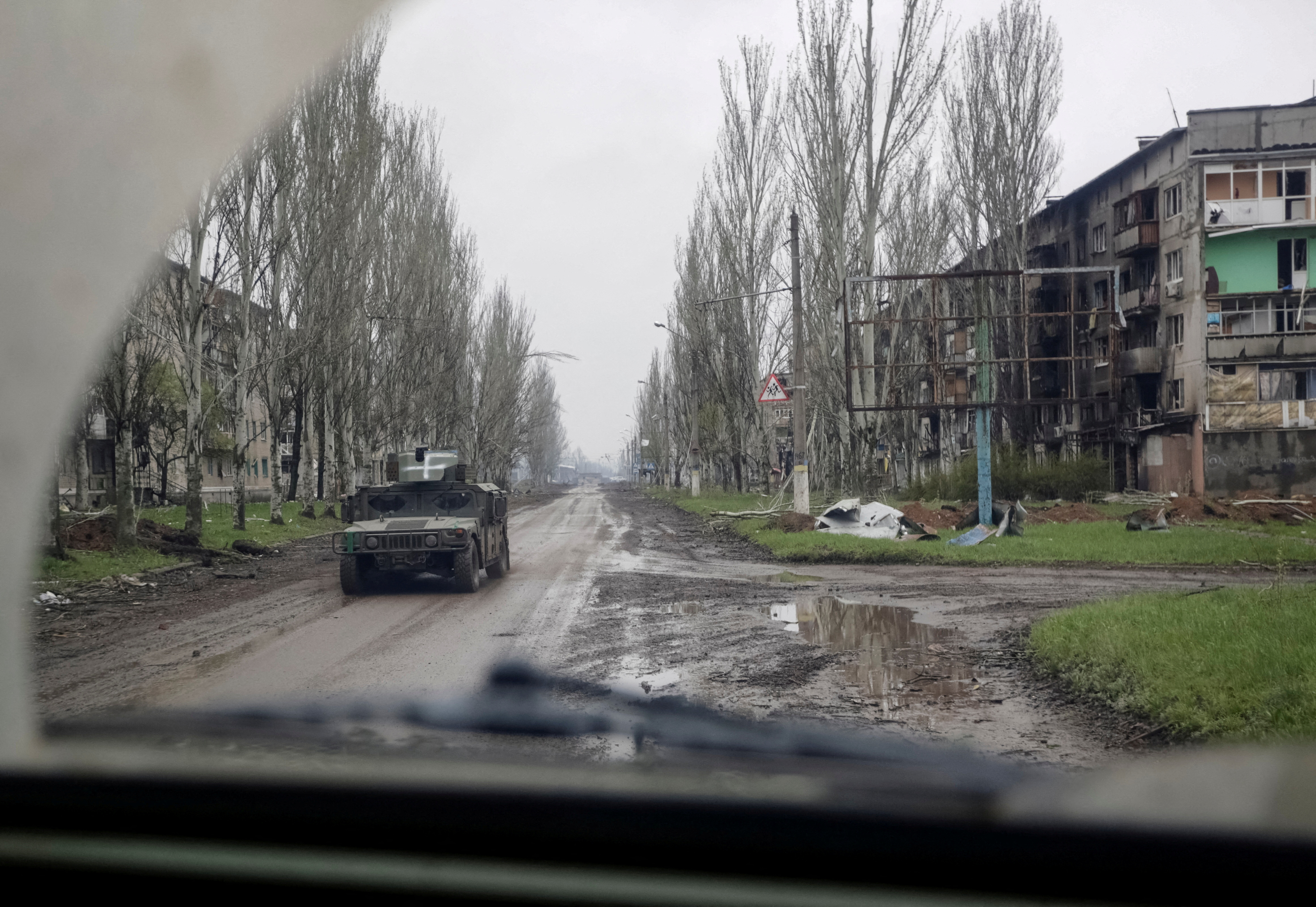 A Ukrainian service member rides a military vehicle near residential buildings damaged by a Russian military strike in the front line town of Bakhmut