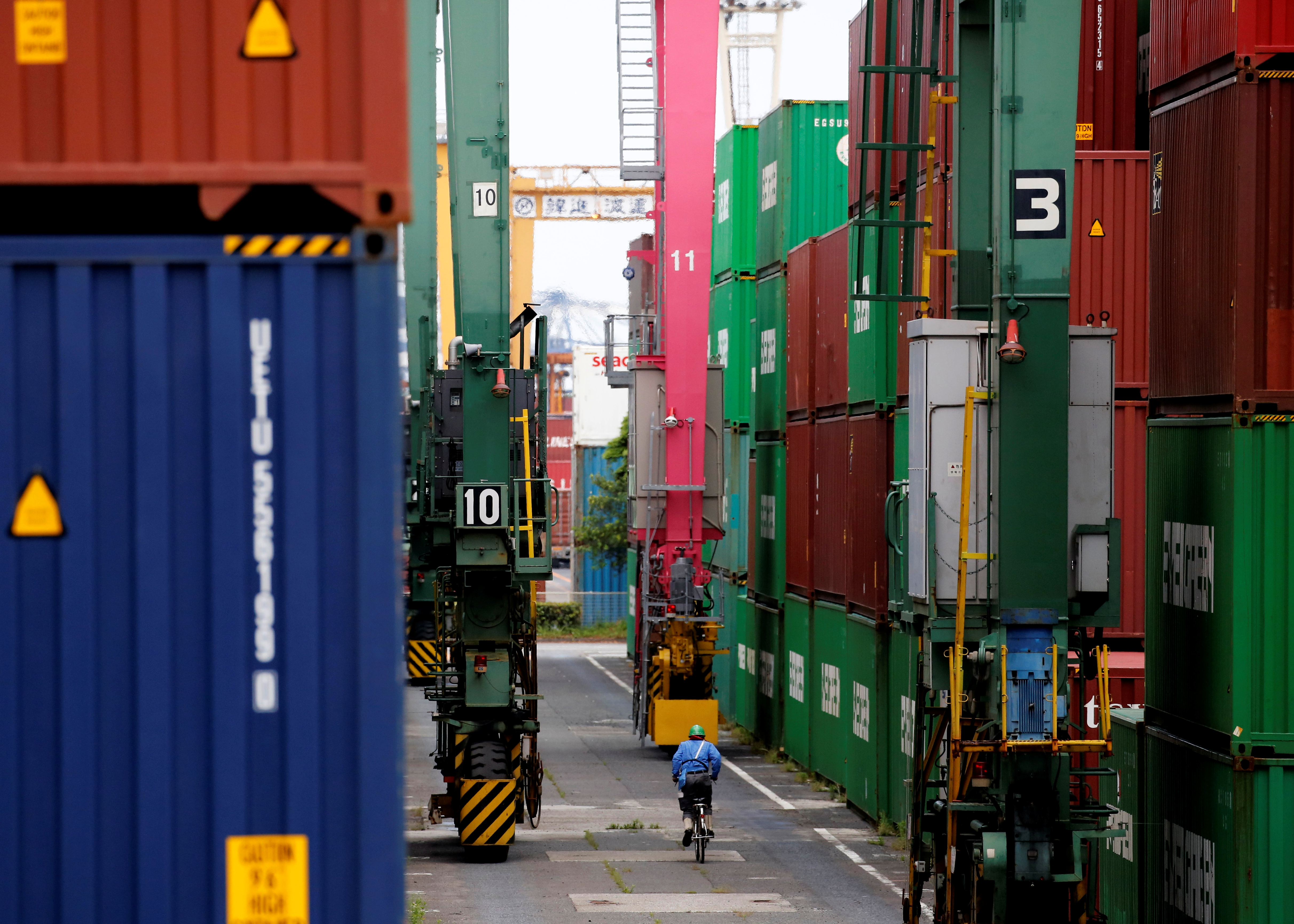 A man in a bicycle drives past containers at an industrial port in Tokyo