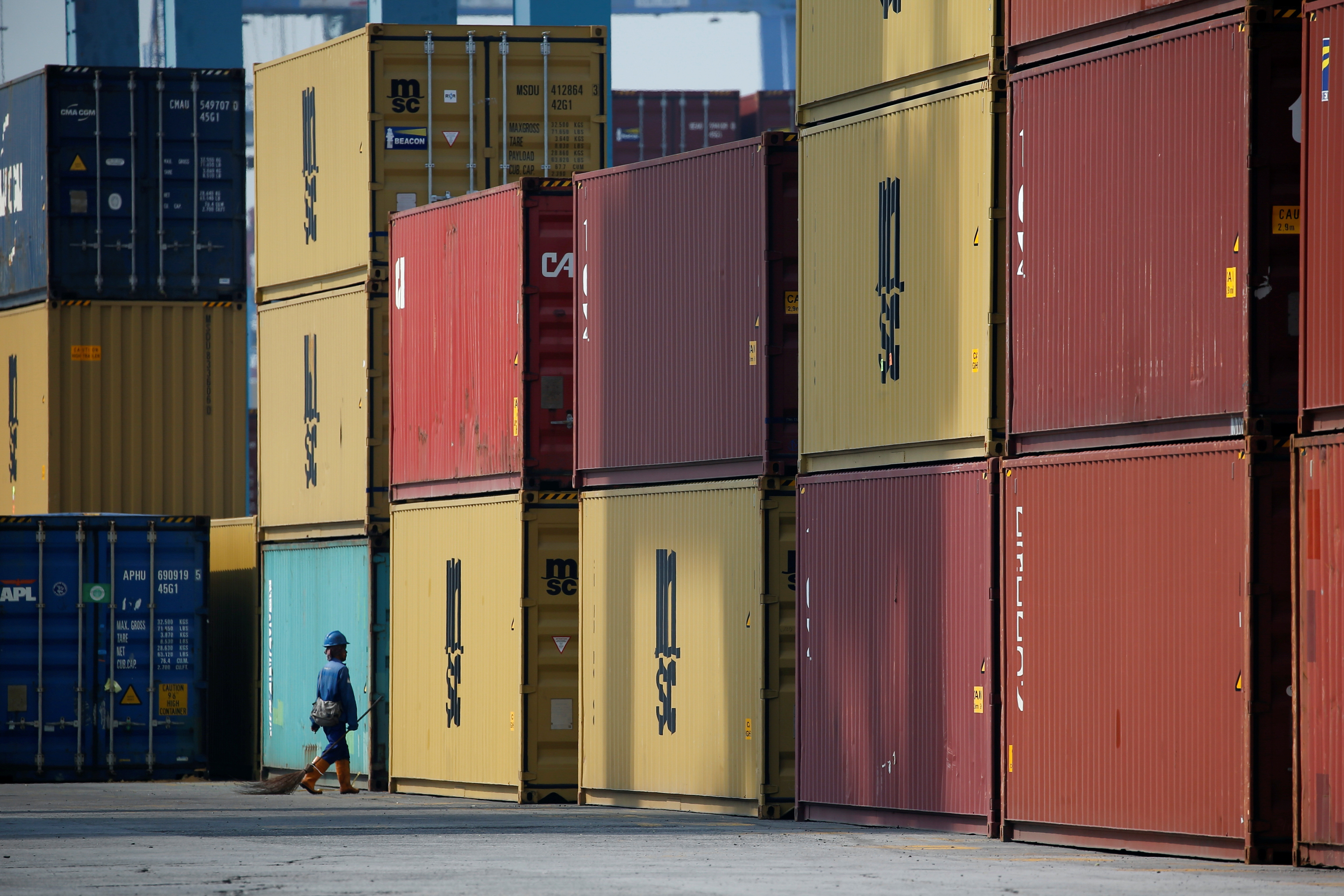 A worker carrying a broom passes stacks of containers at the IPC Containter Terminal of Tanjung Priok port in Jakarta