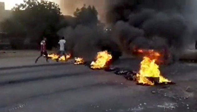 People walk past burning objects lying on the streets of Kartoum, Sudan, amid reports of a coup