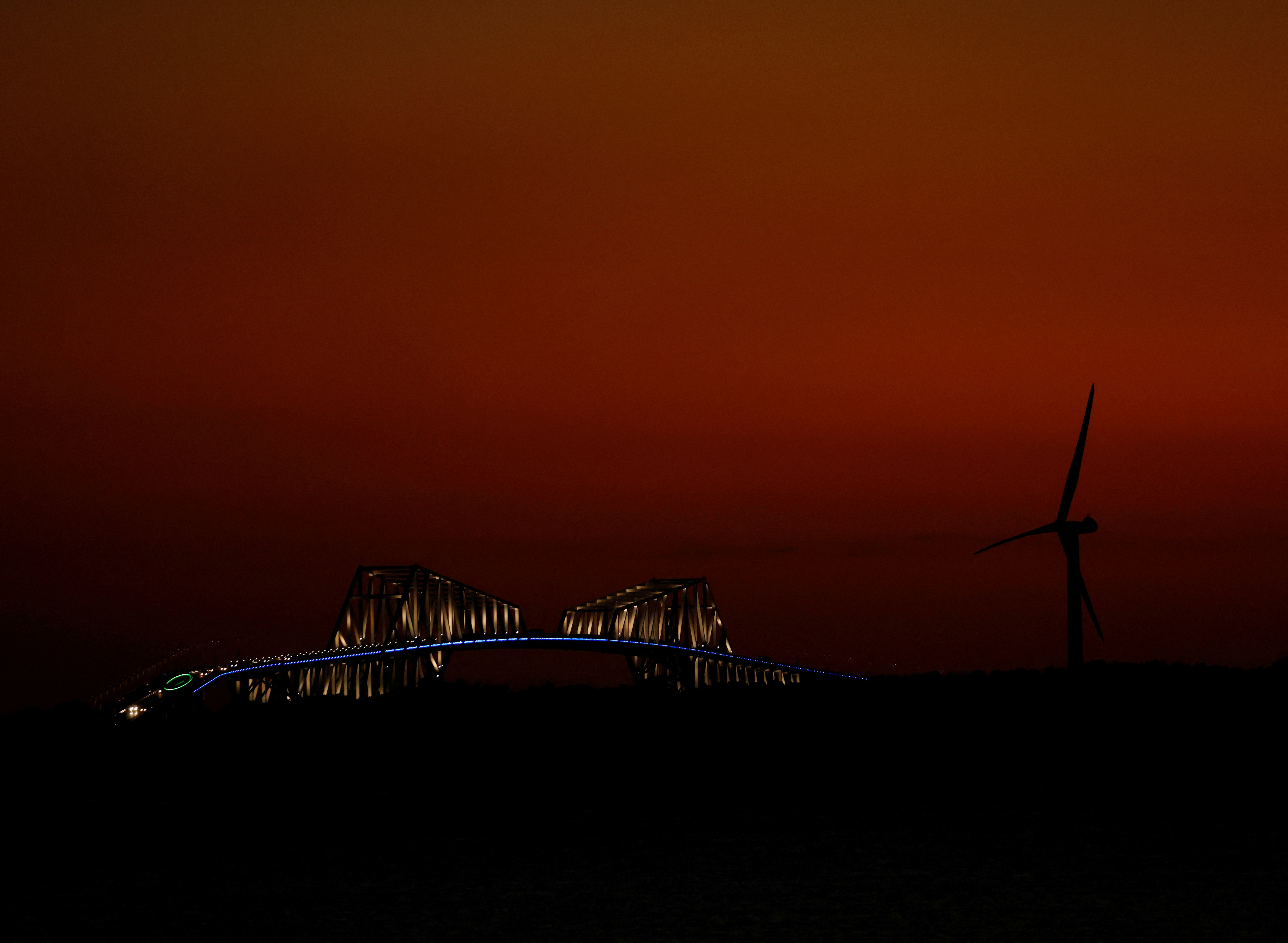 A wind turbine and a bridge are seen during sunset in Tokyo