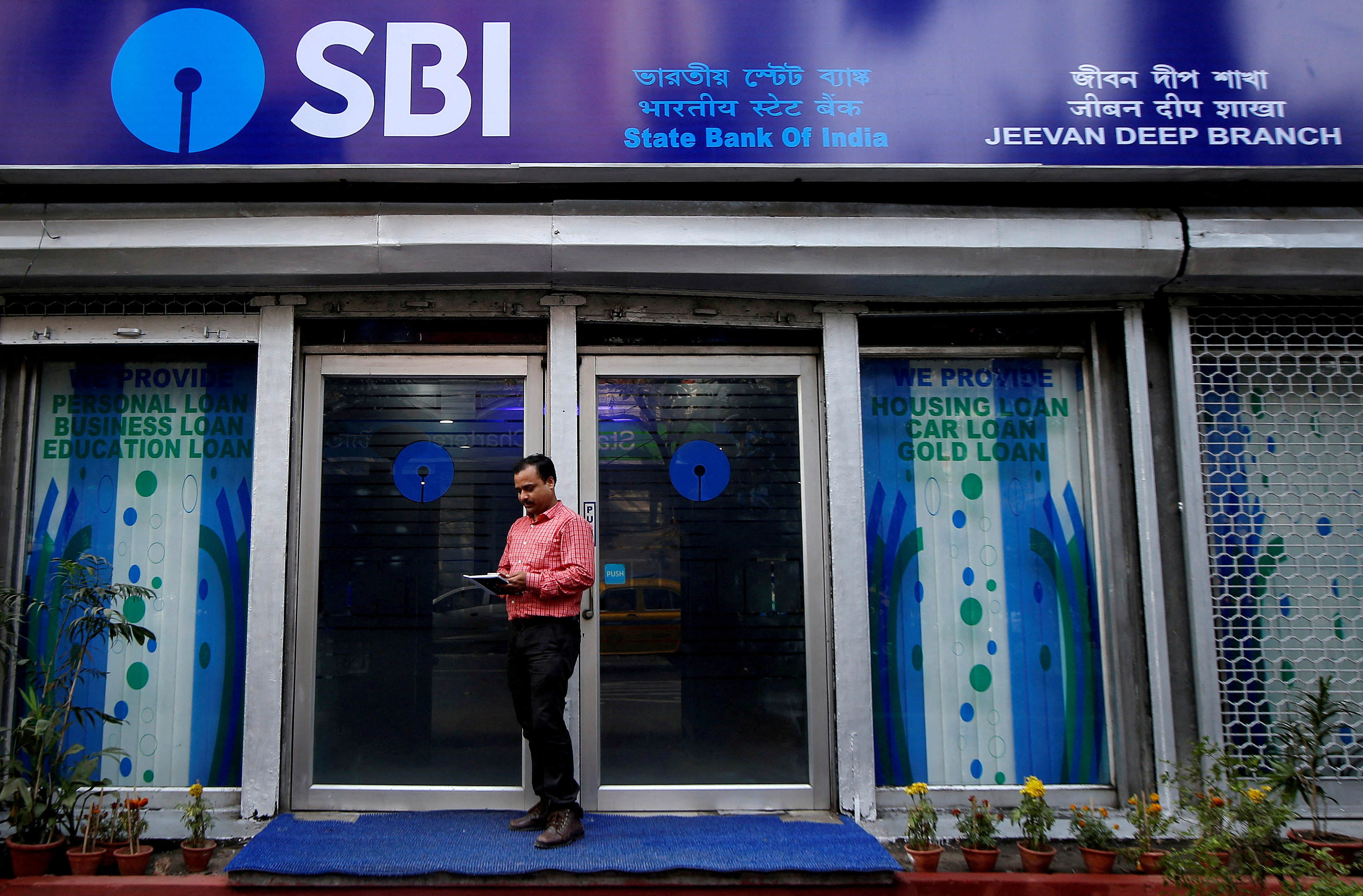 A man checks his mobile phone in front of a State Bank of India (SBI) branch in Kolkata