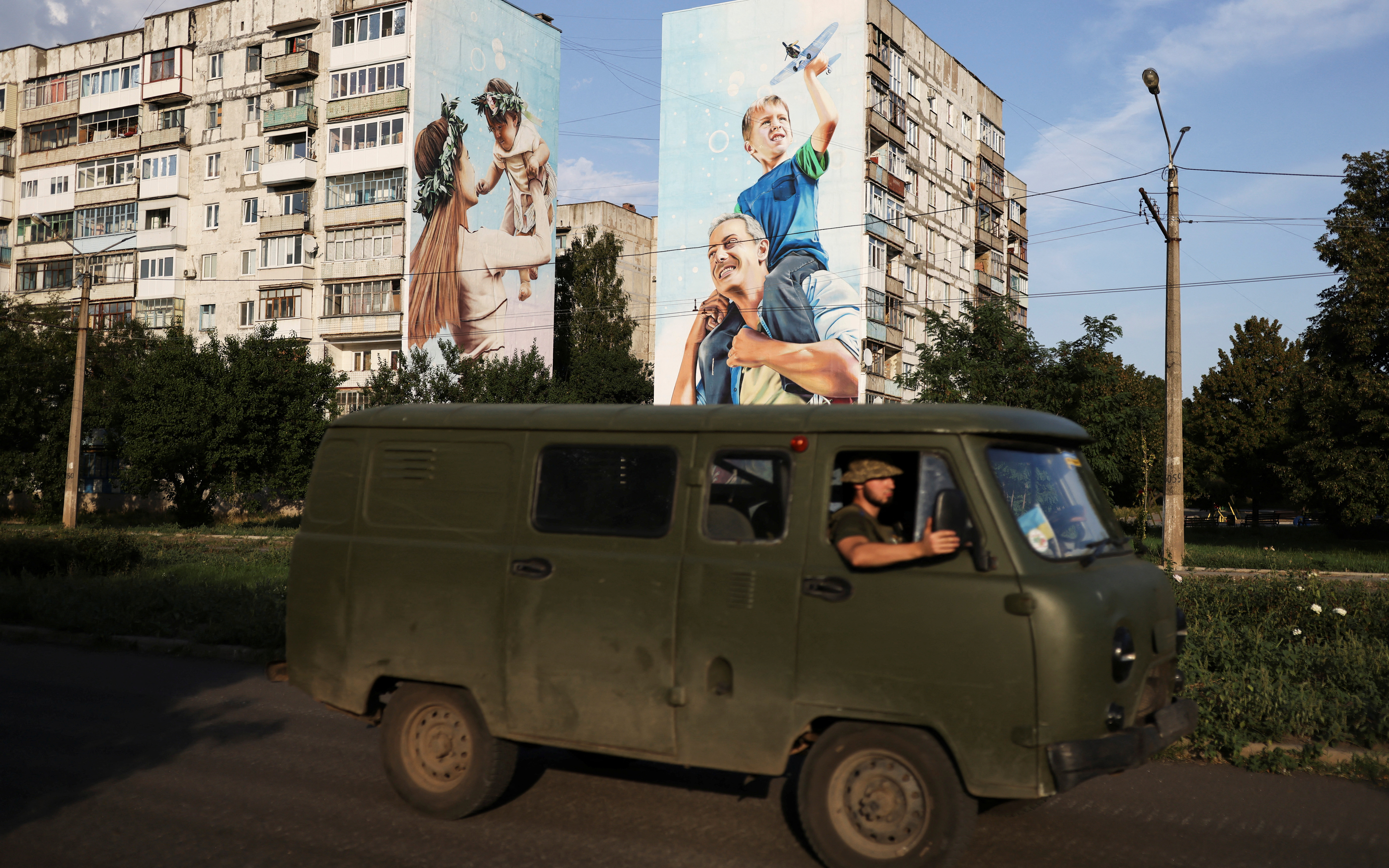 Ukraine servicemen drive past a mural of a family painted on damaged buildings in Bakhmut