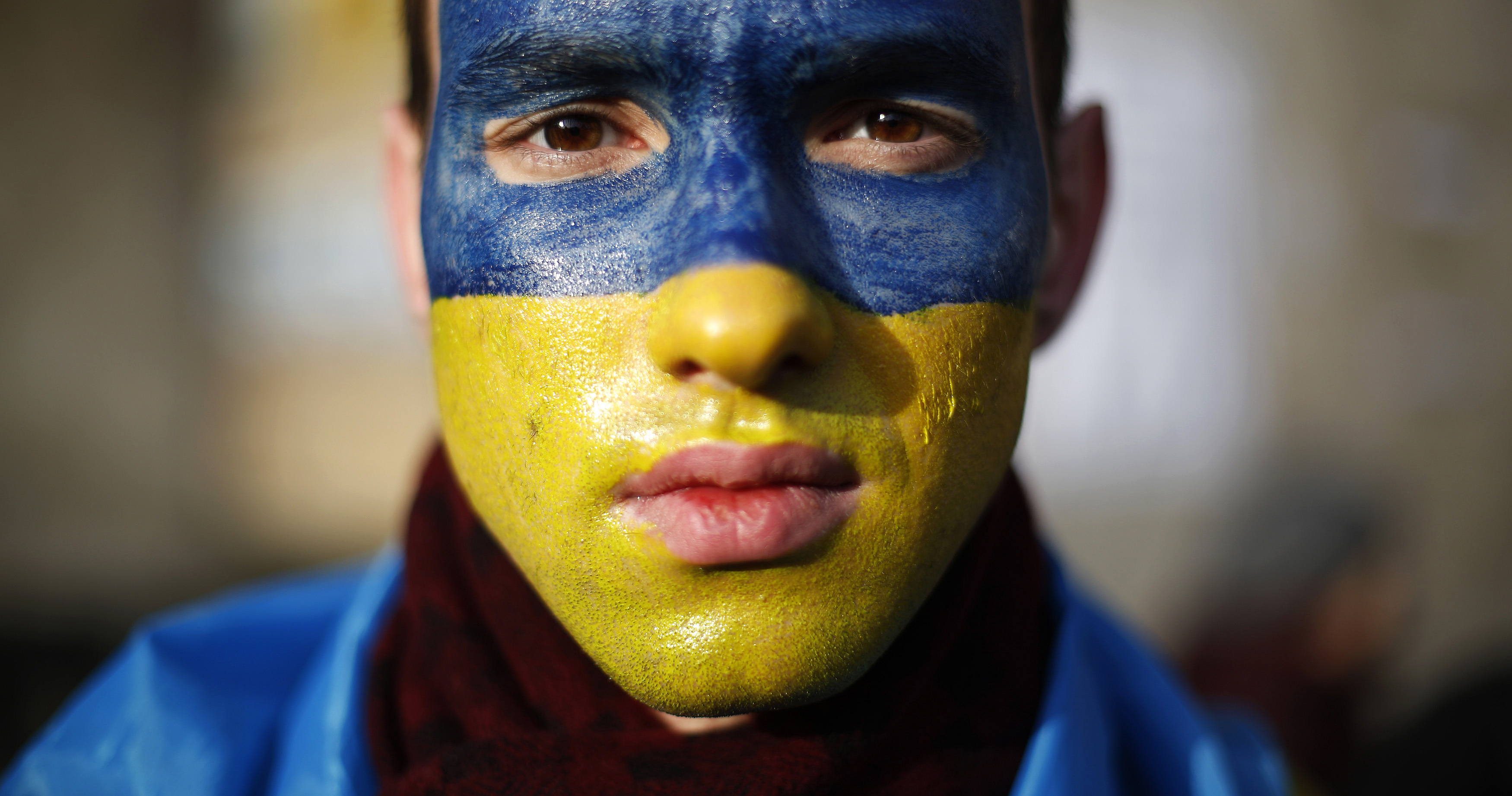 Man with his painted in the colours of the Ukranian flag poses for a portrait at Independence Square in Kiev