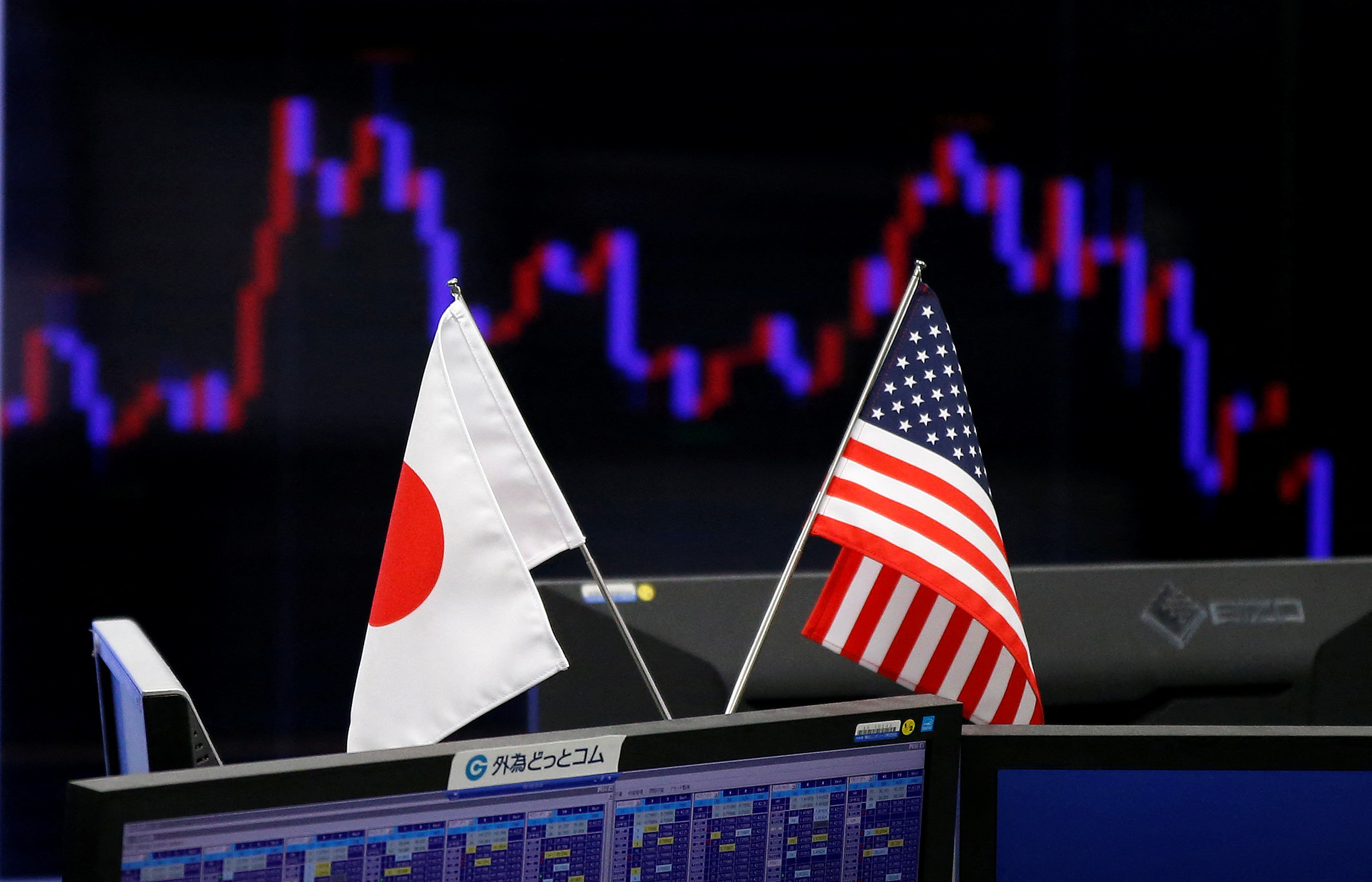National flags of Japan and the U.S. are seen in front of a monitor showing a graph of the Japanese yen's exchange rate against the U.S. dollar at a foreign exchange trading company in Tokyo
