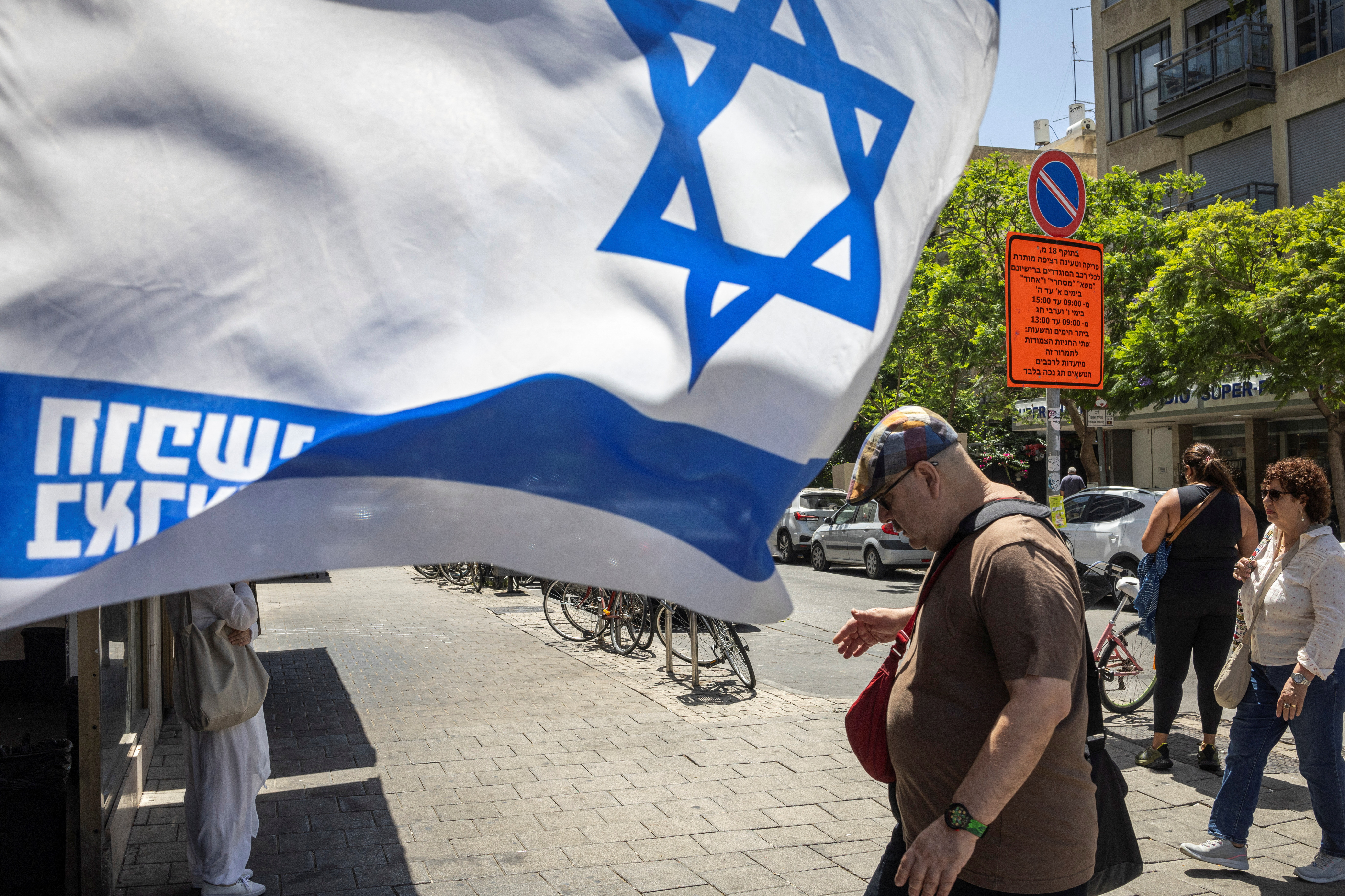 People walk past an Israeli flag, in support of hostages kidnapped during the deadly October 7 attack on Israel by Hamas, amid the ongoing Israel-Hamas conflict, in Tel Aviv