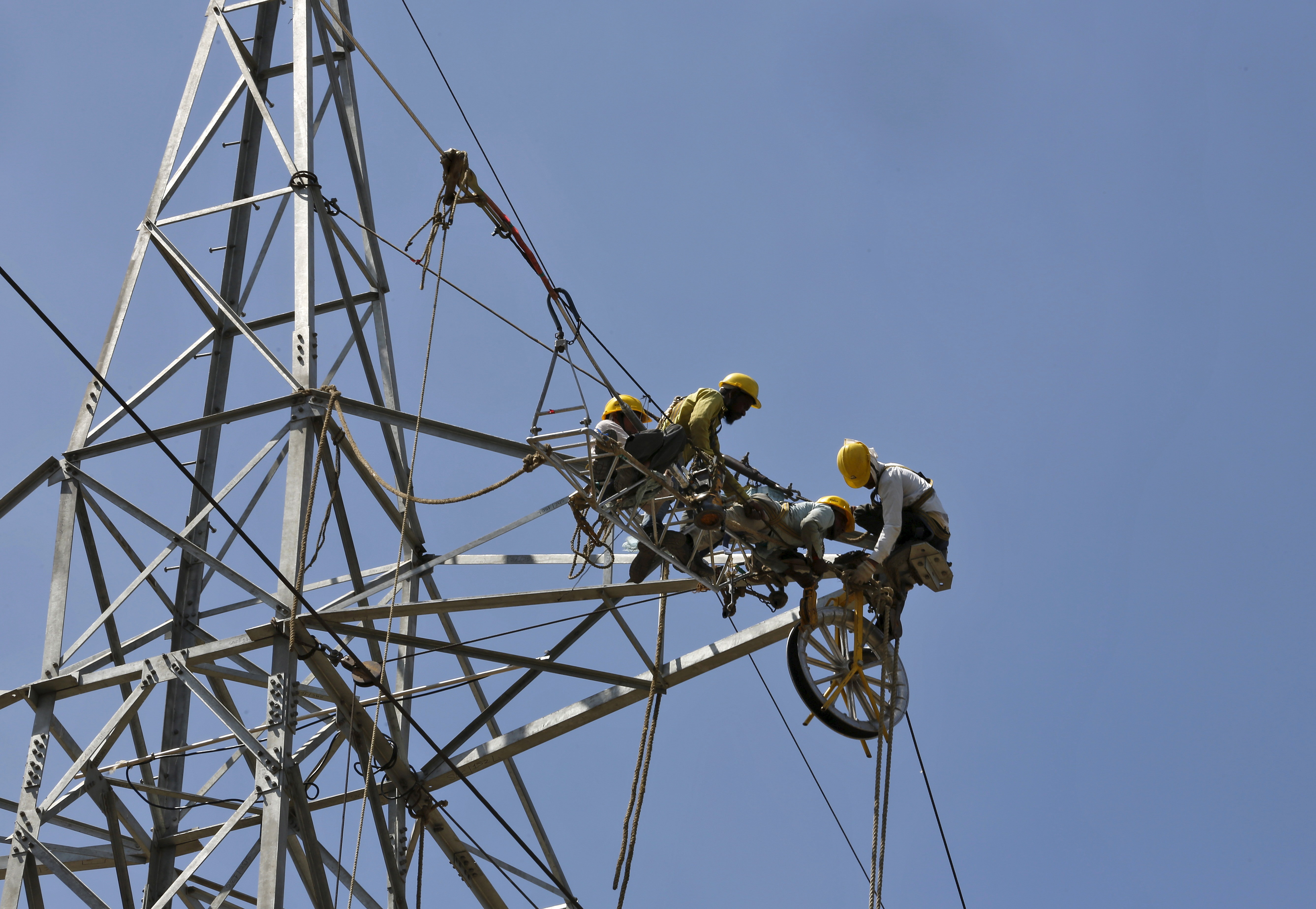 Workers of Torrent Power Limited install cables on electric pylon on the outskirts Ahmedabad