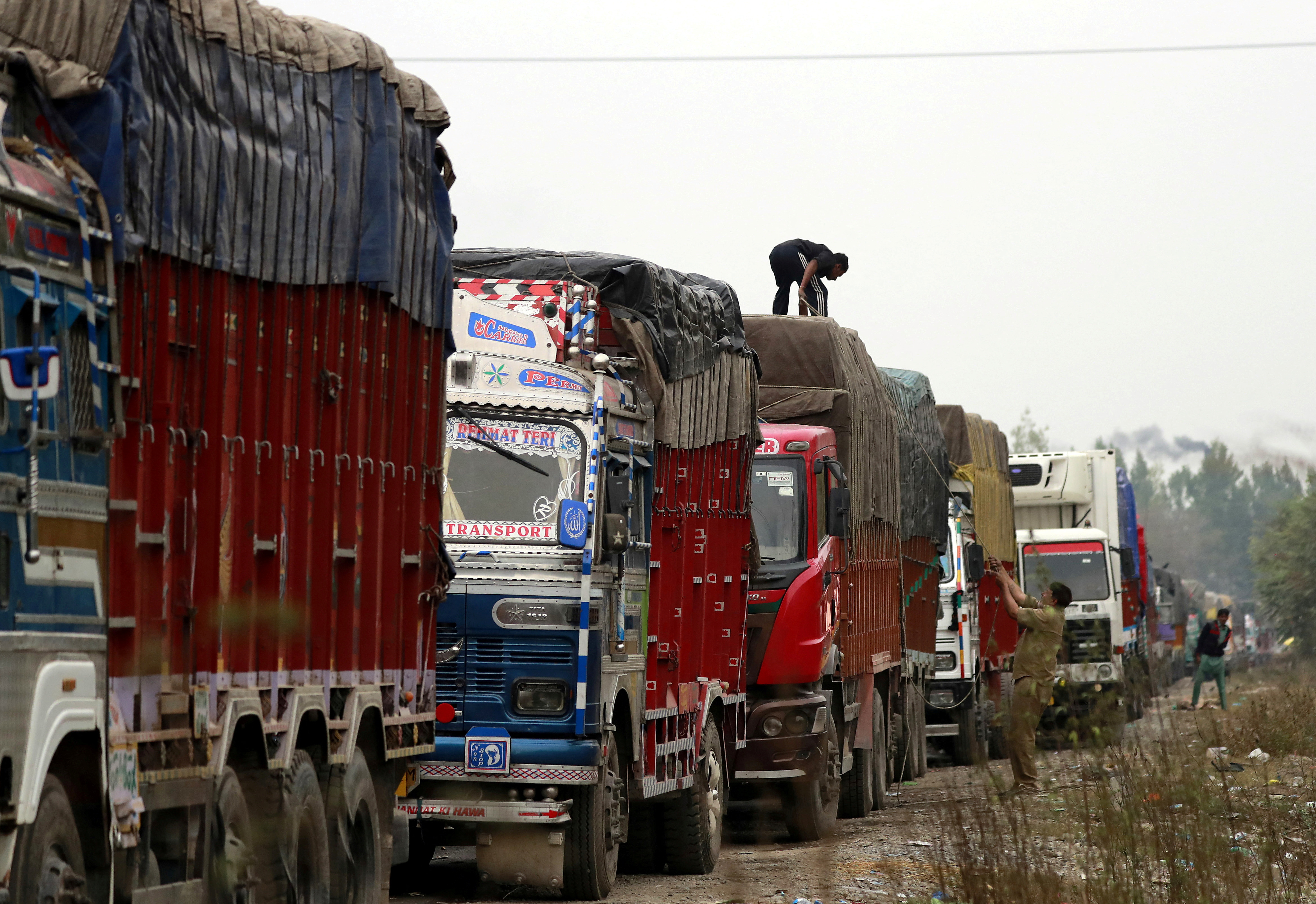 A driver covers a supply truck loaded with apples on a highway near Qazigund