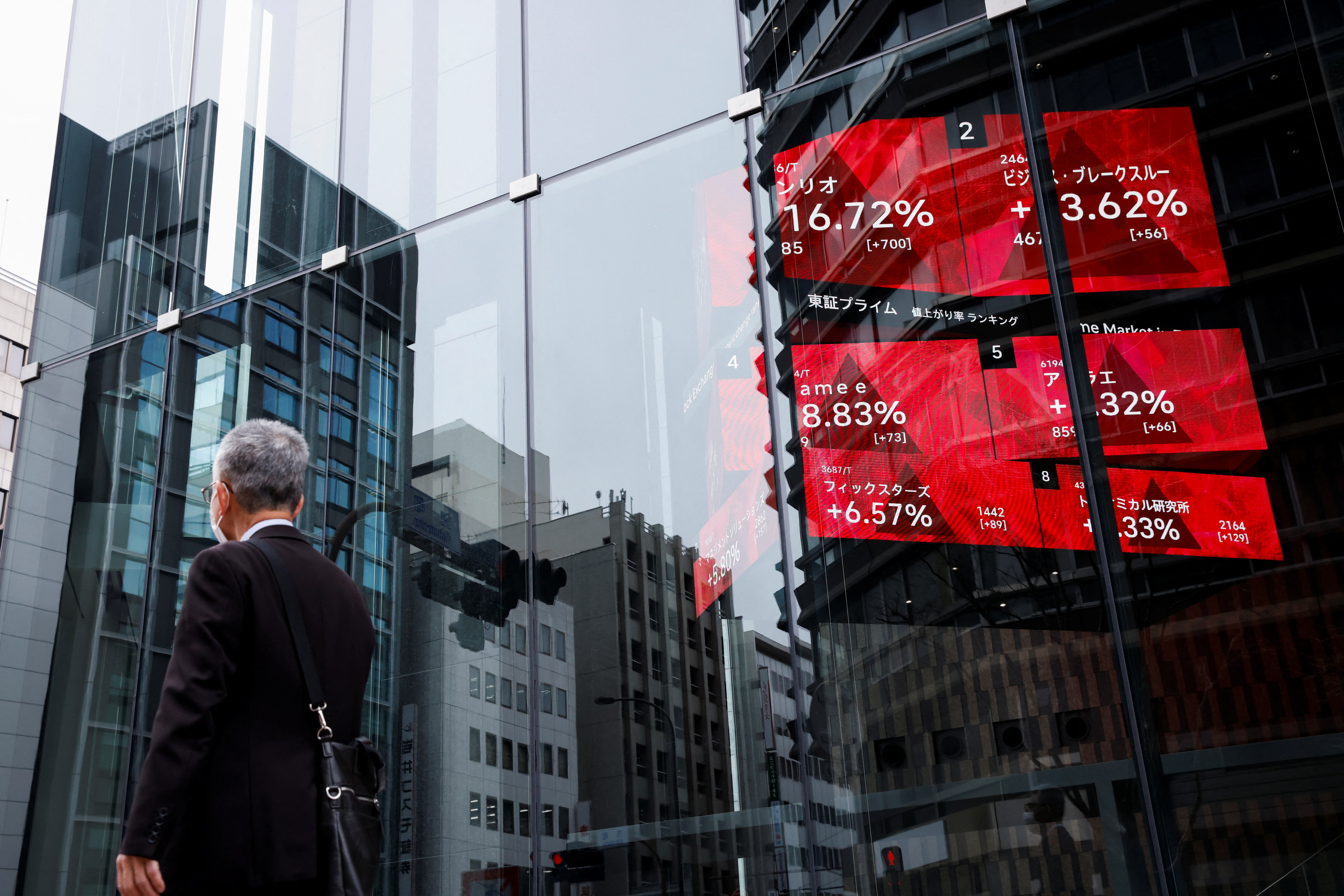 A man walks past an electronic board showing stock visualizations outside a brokerage, in Tokyo