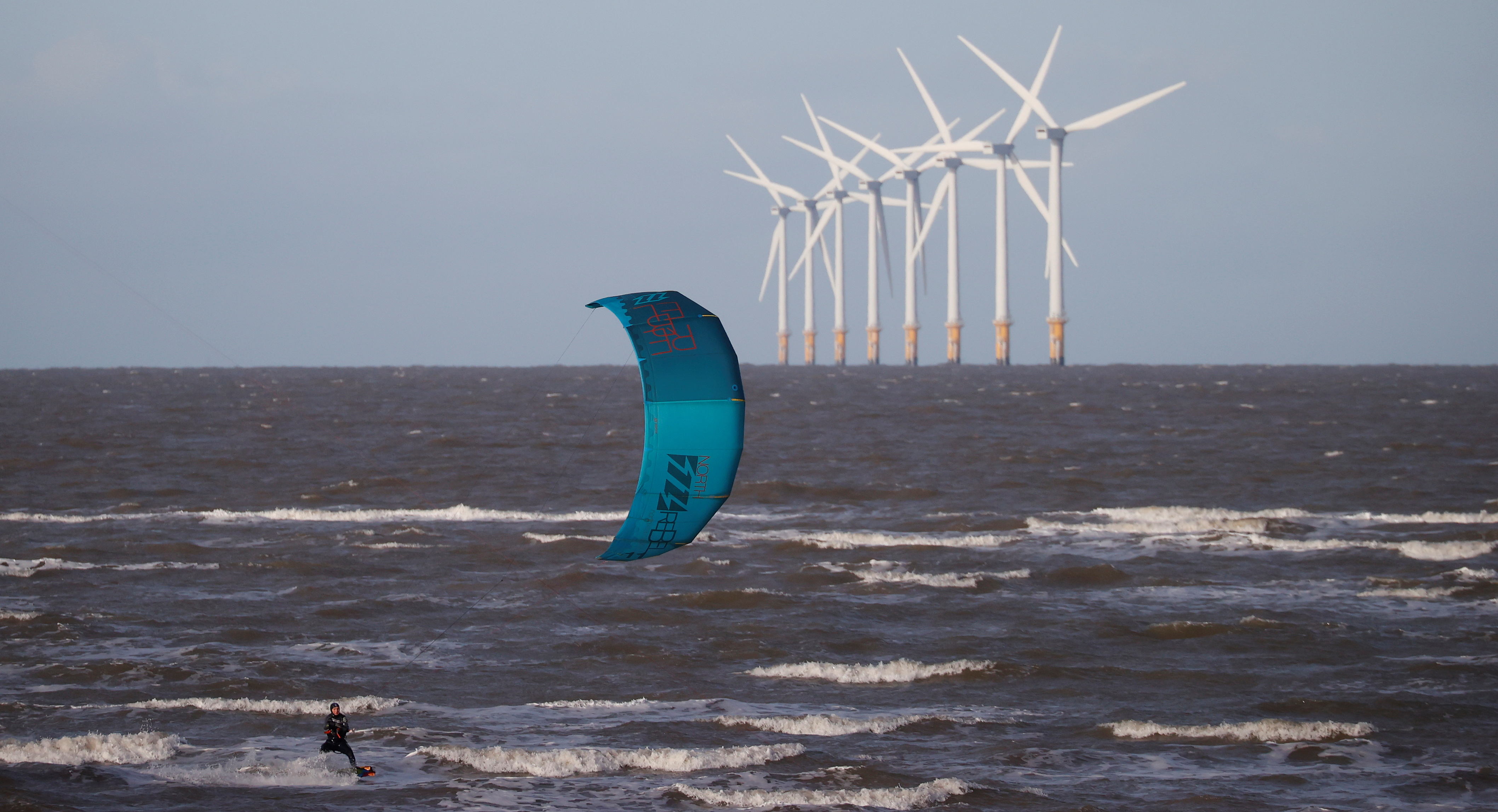 A kitesurfer rides the waves in front of the Burbo Bank offshore wind farm near Wallasey