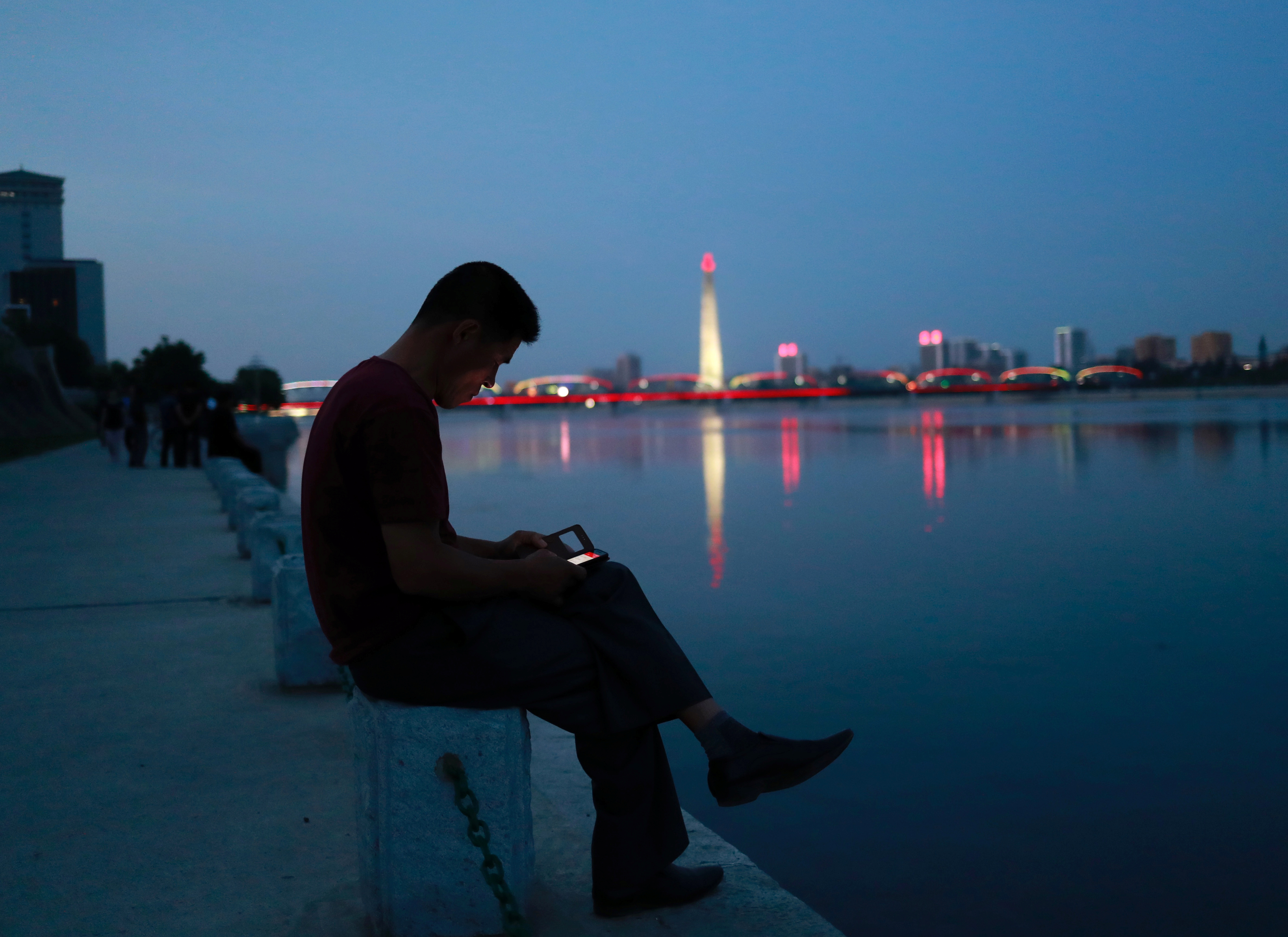 A man uses his phone as he sits along the Taedong river in Pyongyang